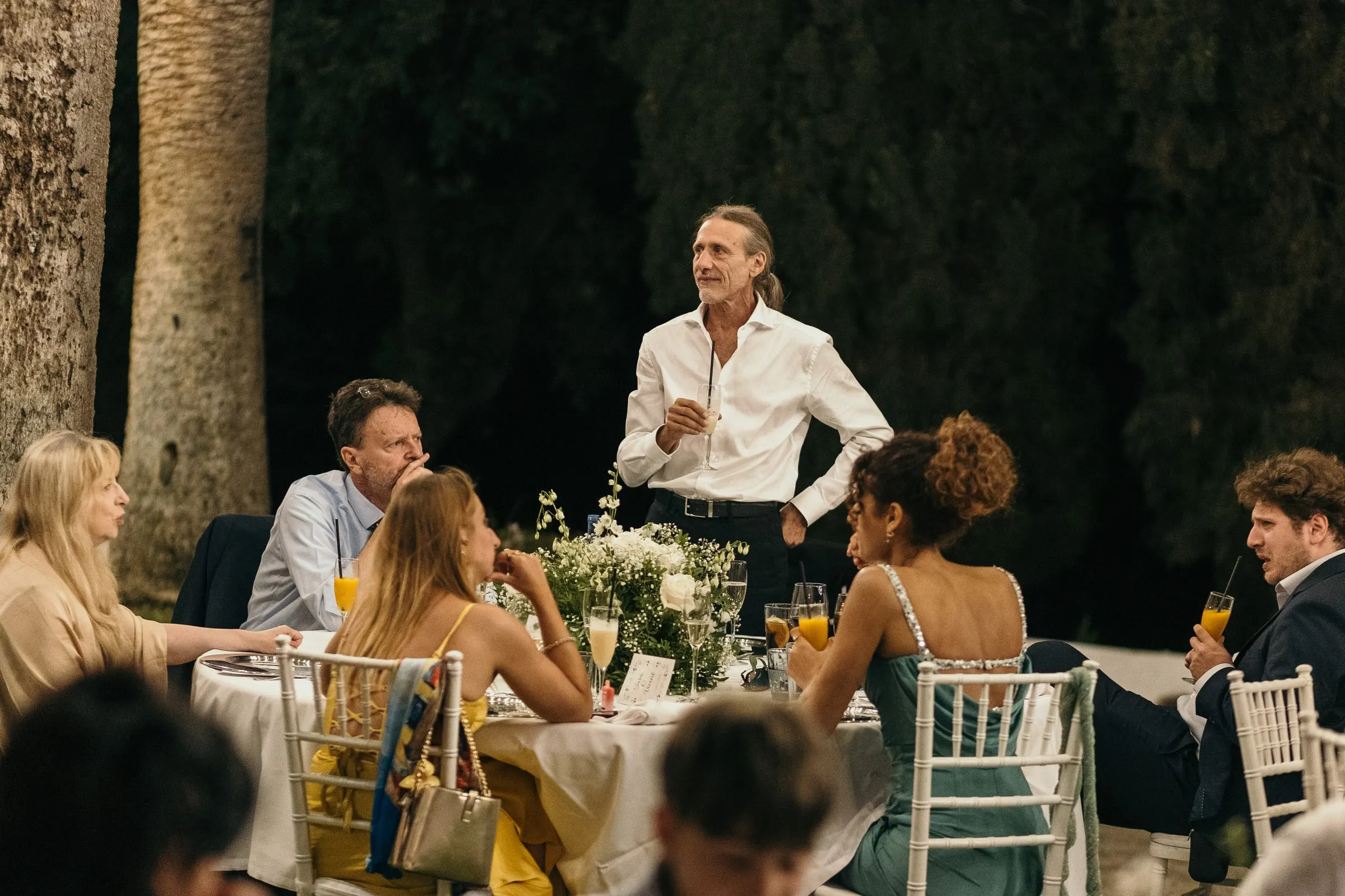Un invitado da un discurso de noche entre las mesas de la cena