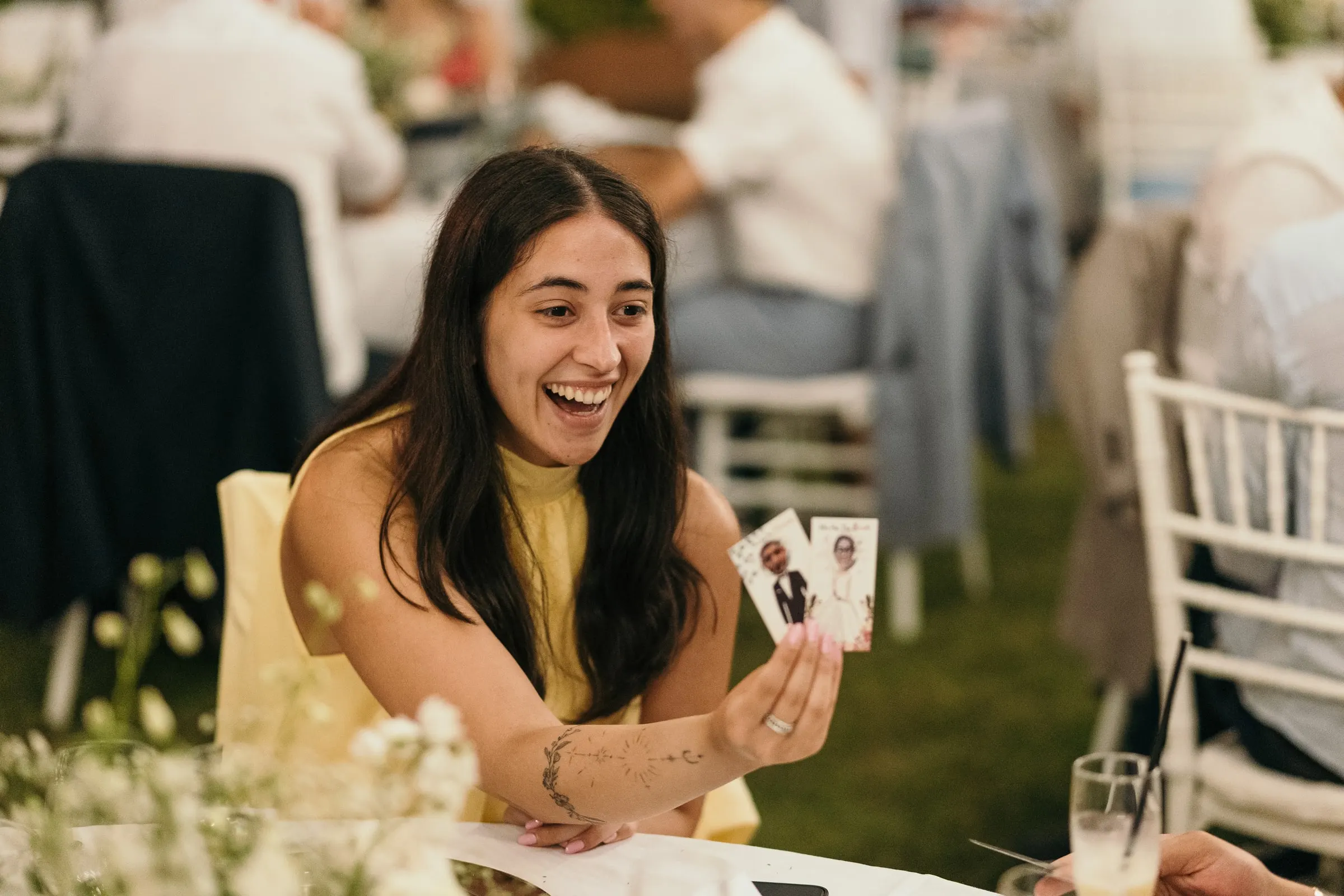 Una invitada se ríe mientras enseña una tarjeta con una foto en la cena