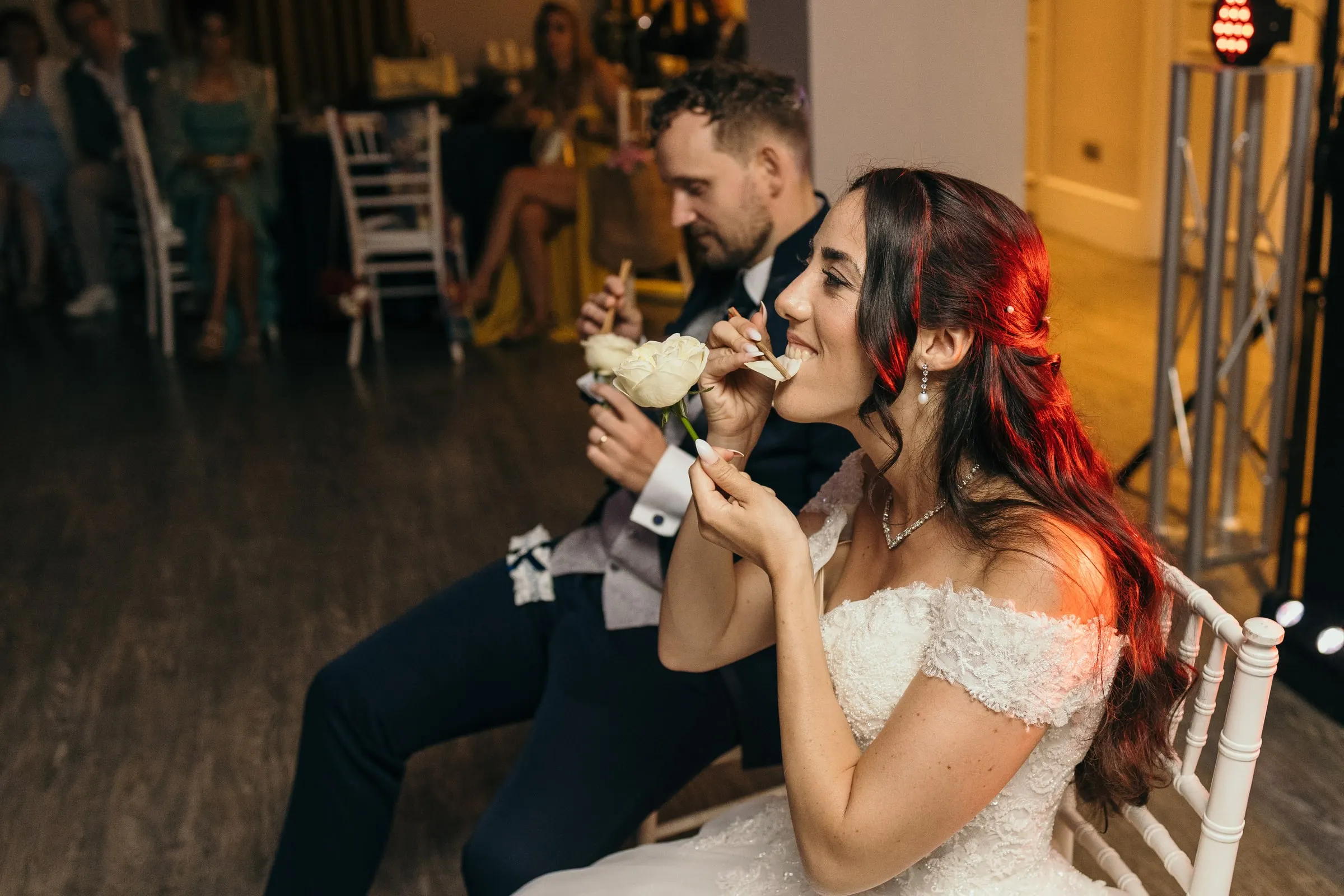 Sara se ríe sentada en una silla con Vincent al lado en el salón de la fiesta