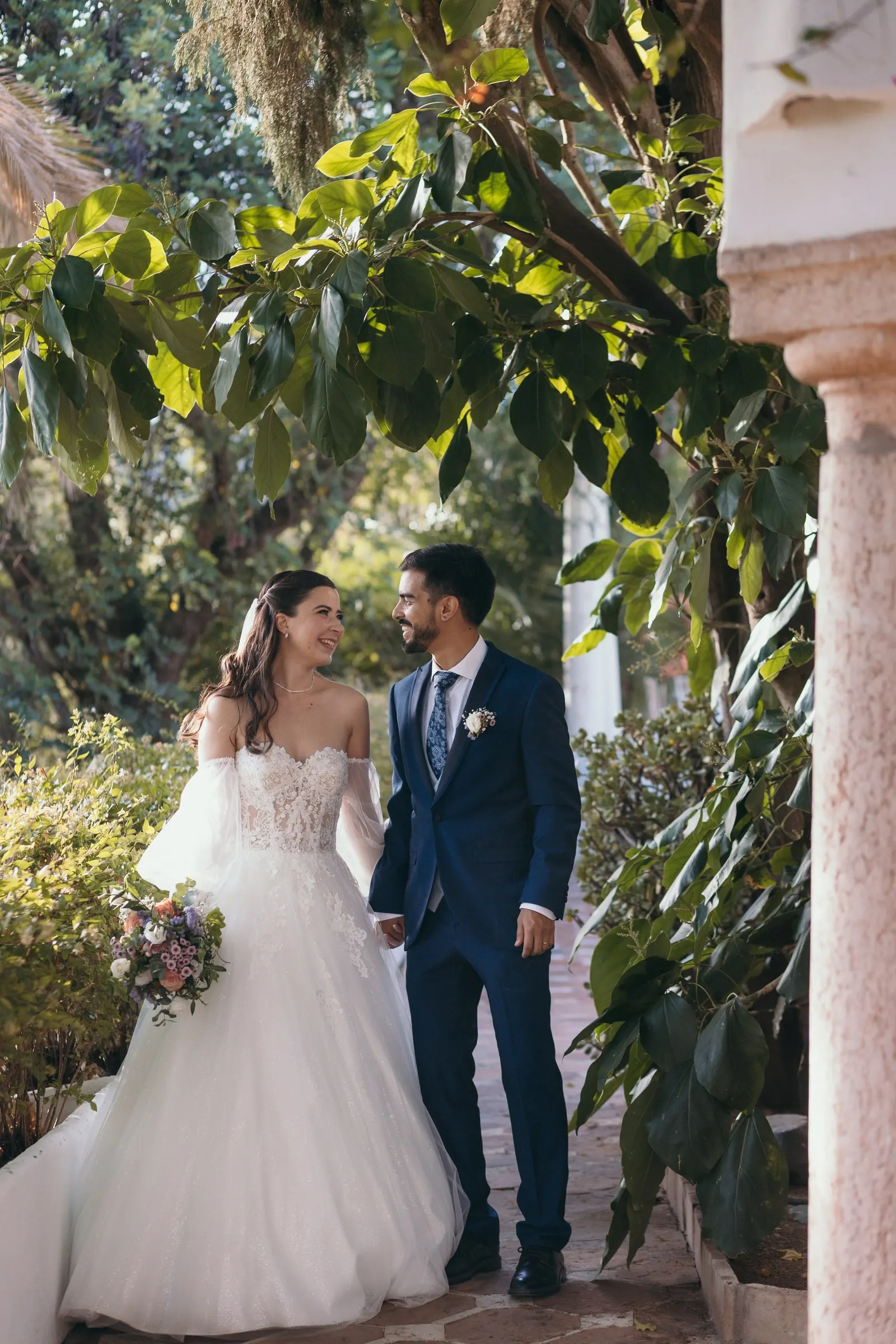 Los novios, de la mano bajo una arcada del jardín rodeada de plantas, Cortijo San Francisco, Estepona