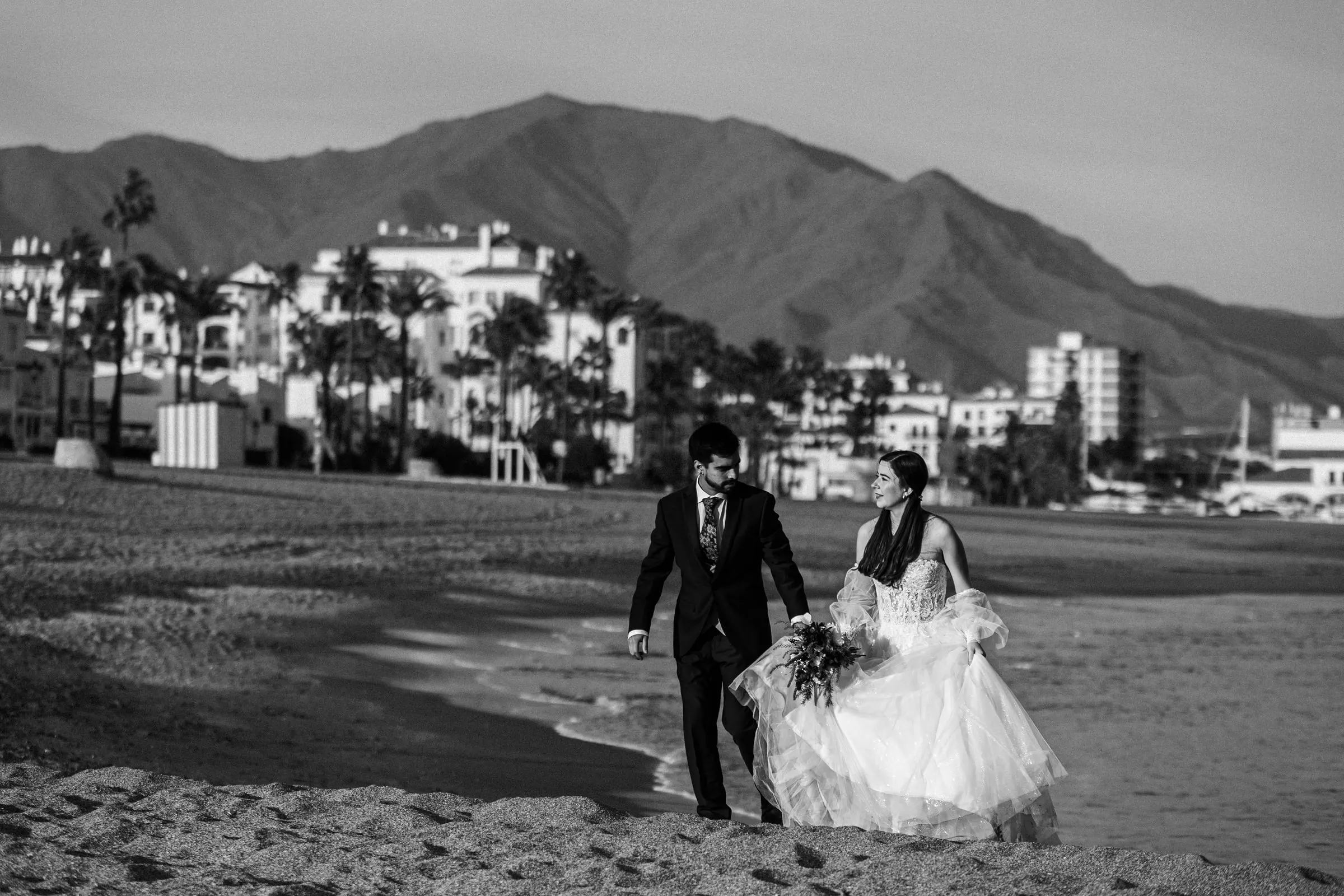 Los novios pasean por la orilla en blanco y negro, con la sierra al fondo, Cortijo San Francisco, Estepona