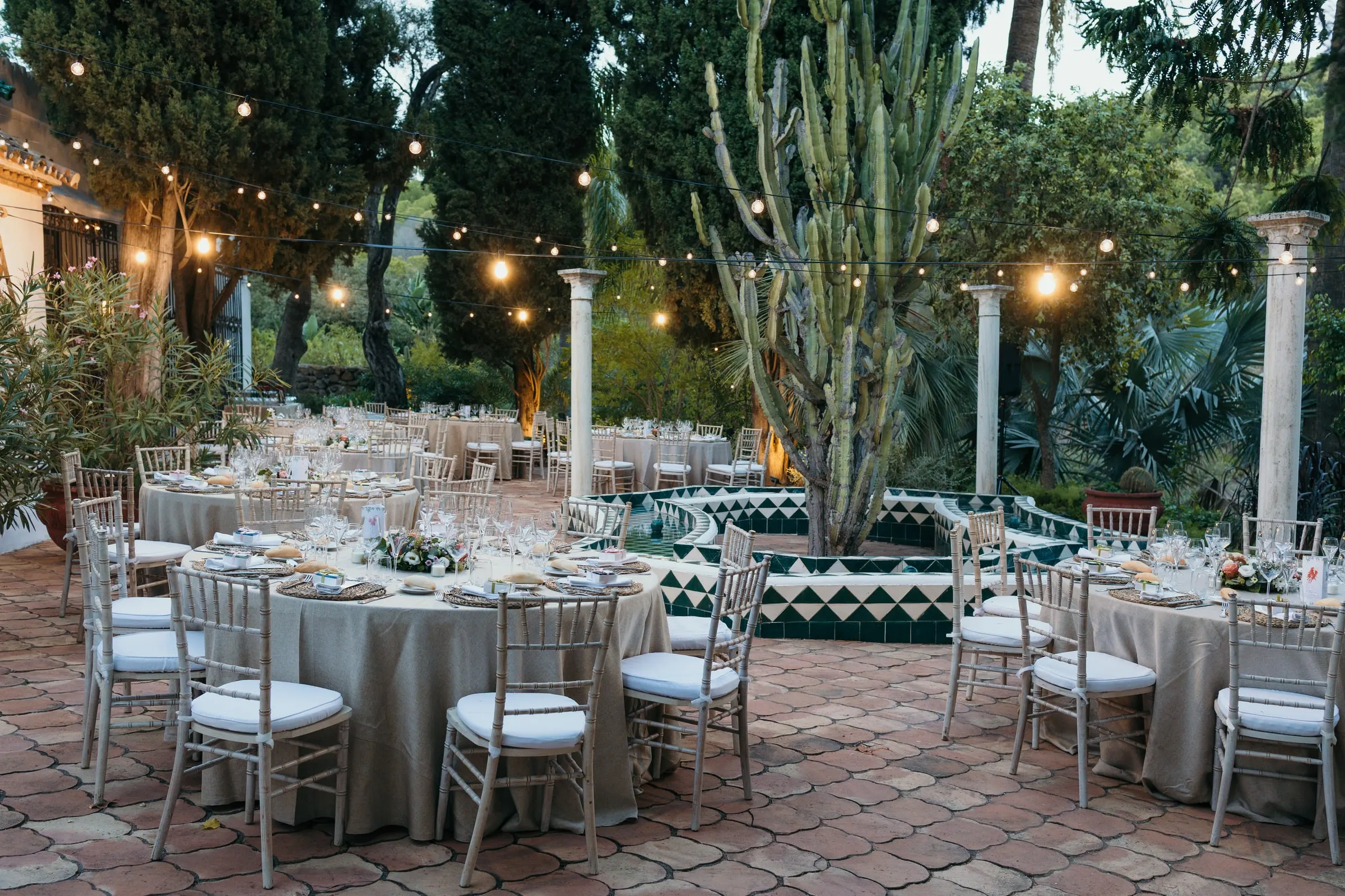 Mesas del banquete en el patio de baldosas, entre guirnaldas de luces y cactus, Cortijo San Francisco, Estepona