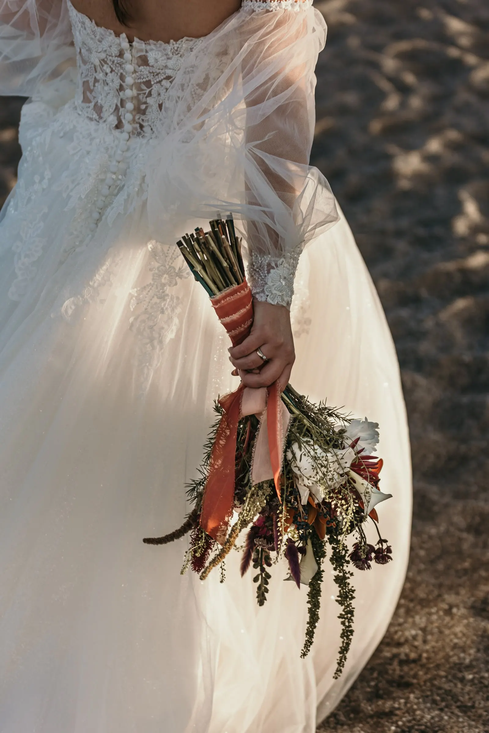 Bride holding her dried-flower bouquet with orange ribbons against her gown, Cortijo San Francisco, Estepona