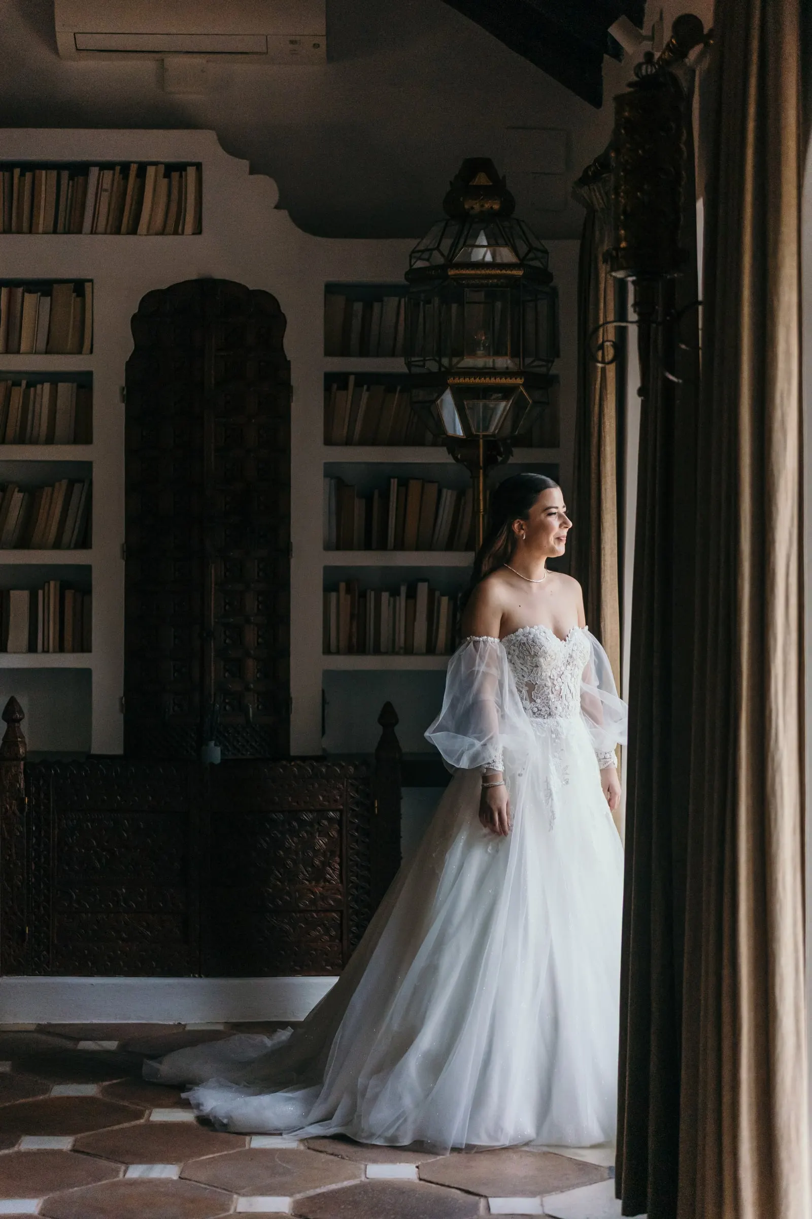 Bride in her gown gazing out of the window in a book-lined room, Cortijo San Francisco, Estepona