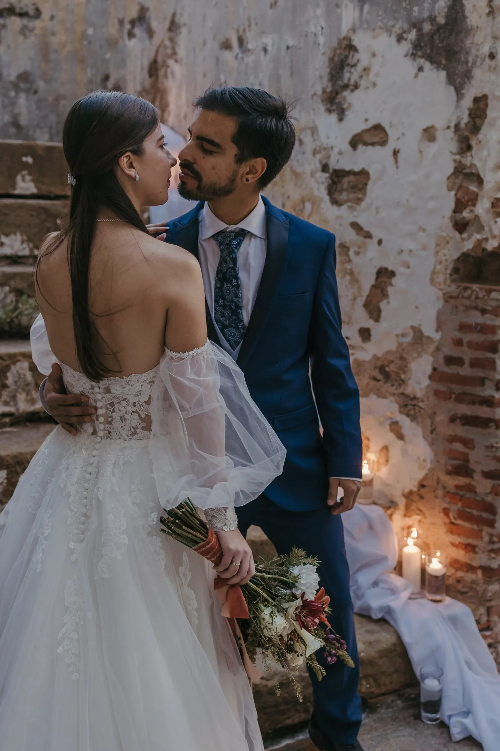 Groom kissing the bride beside a weathered wall lit by candles, Cortijo San Francisco, Estepona