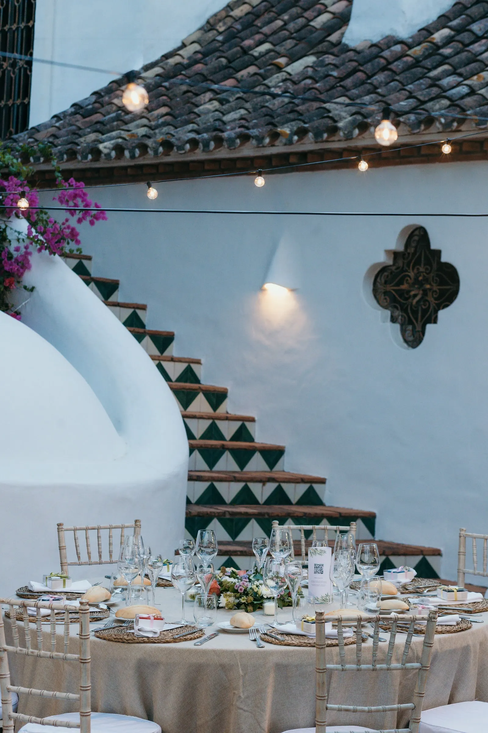 Round table laid beside a white wall with a tiled staircase and fairy lights, Cortijo San Francisco, Estepona