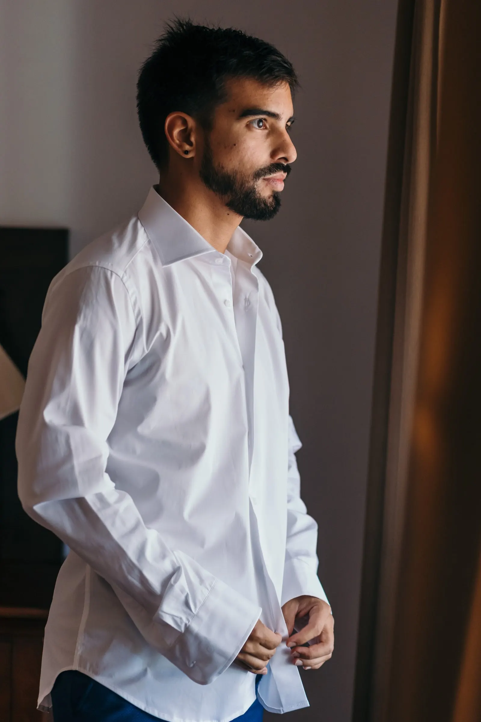 Groom buttoning his white shirt by the window as he gets ready, Cortijo San Francisco, Estepona