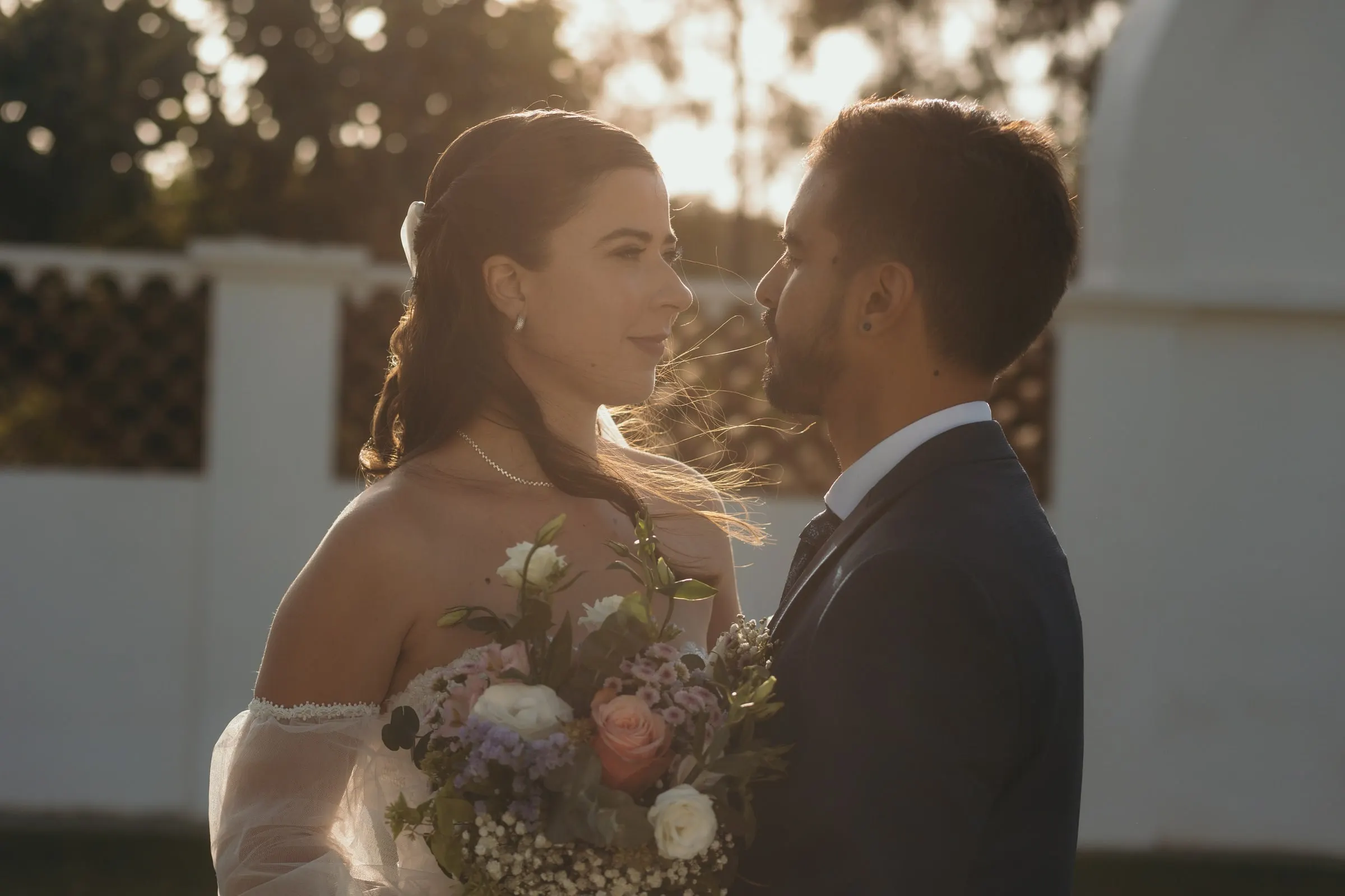 Los novios se miran a contraluz, con la luz dorada de la tarde junto a una tapia blanca, Cortijo San Francisco, Estepona