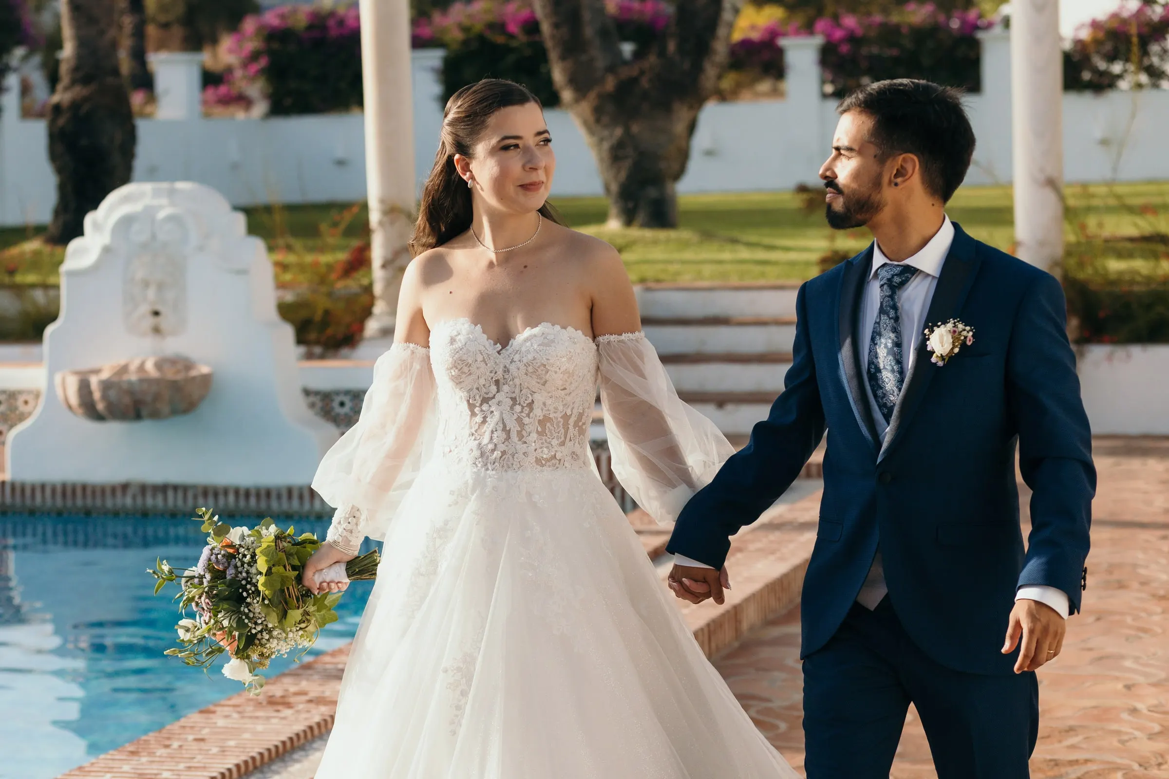 Los novios pasean de la mano junto a la piscina y su fuente de azulejos, Cortijo San Francisco, Estepona