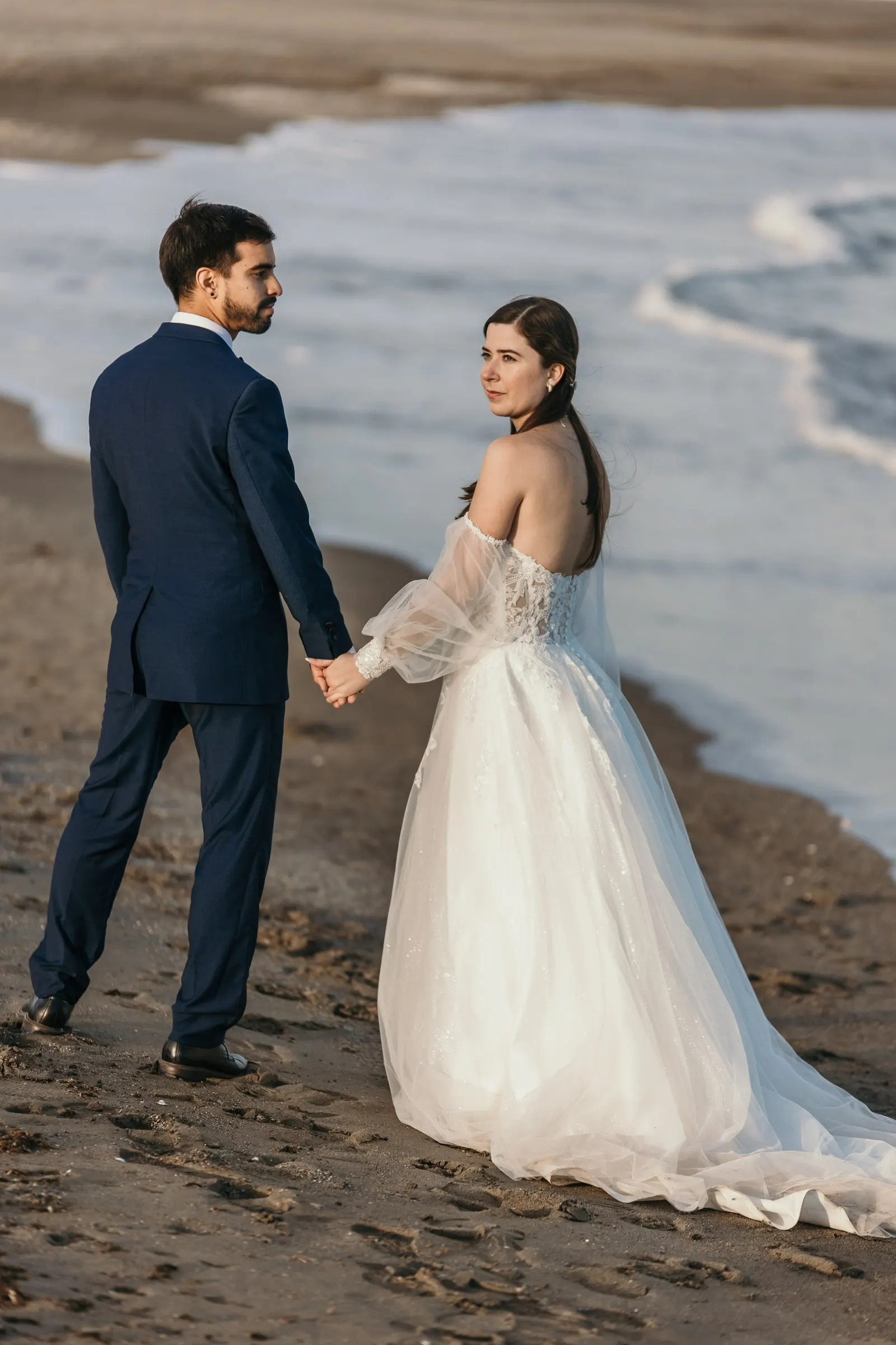 Los novios de la mano en la arena mientras la novia mira hacia atrás, Cortijo San Francisco, Estepona