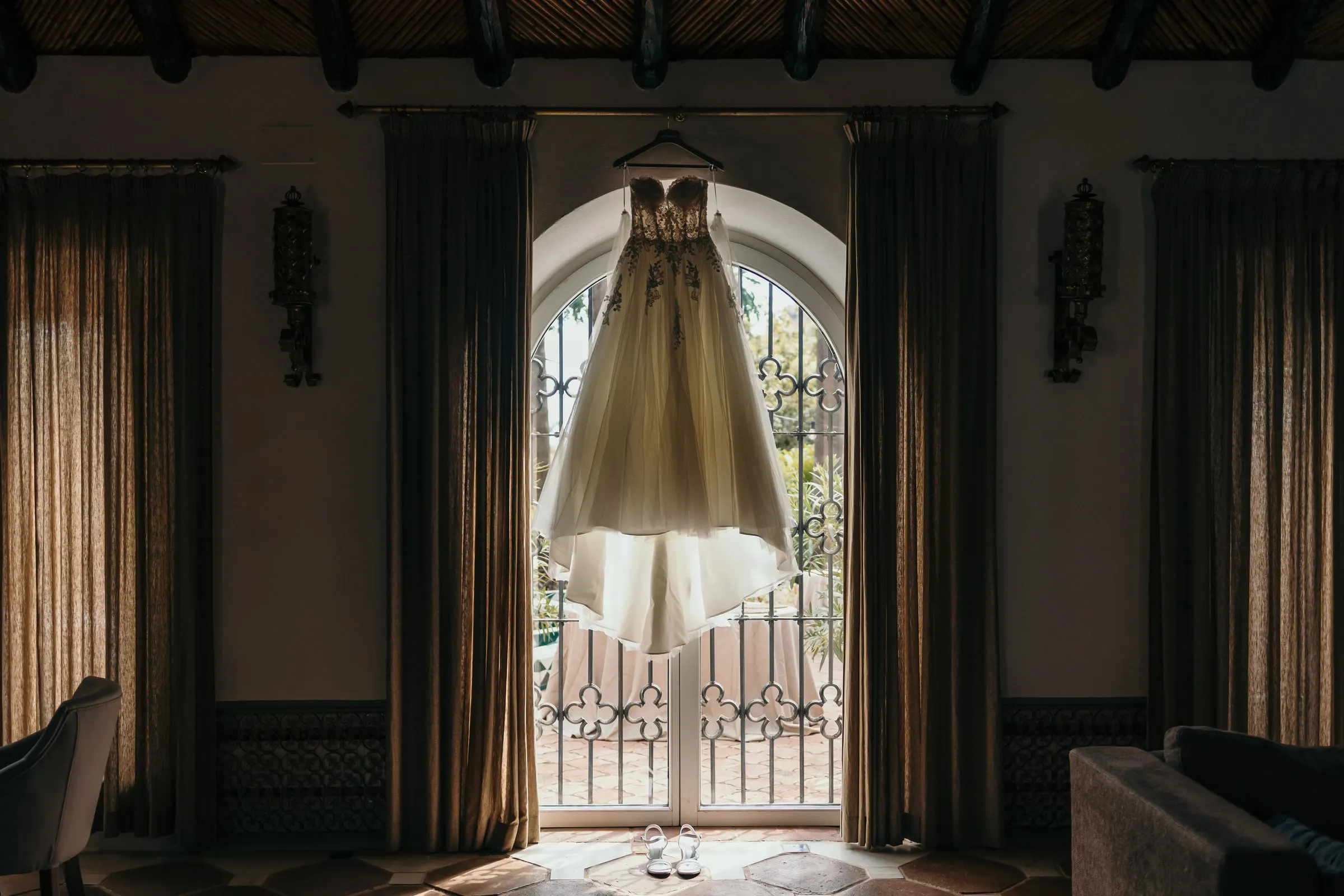El vestido de novia colgado en una ventana en arco, entre cortinas pesadas, Cortijo San Francisco, Estepona