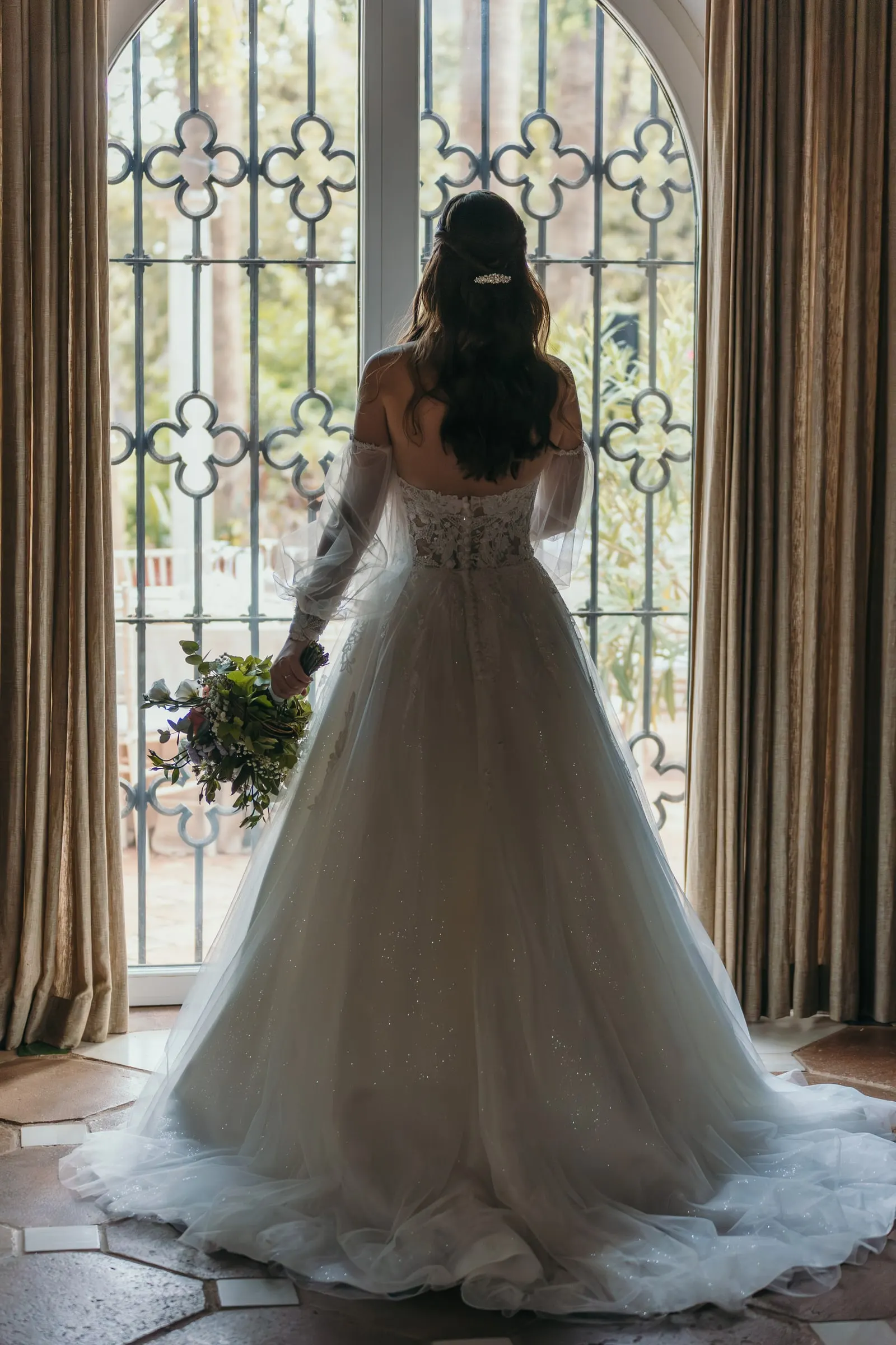 La novia de espaldas con su ramo ante un ventanal de rejería, Cortijo San Francisco, Estepona