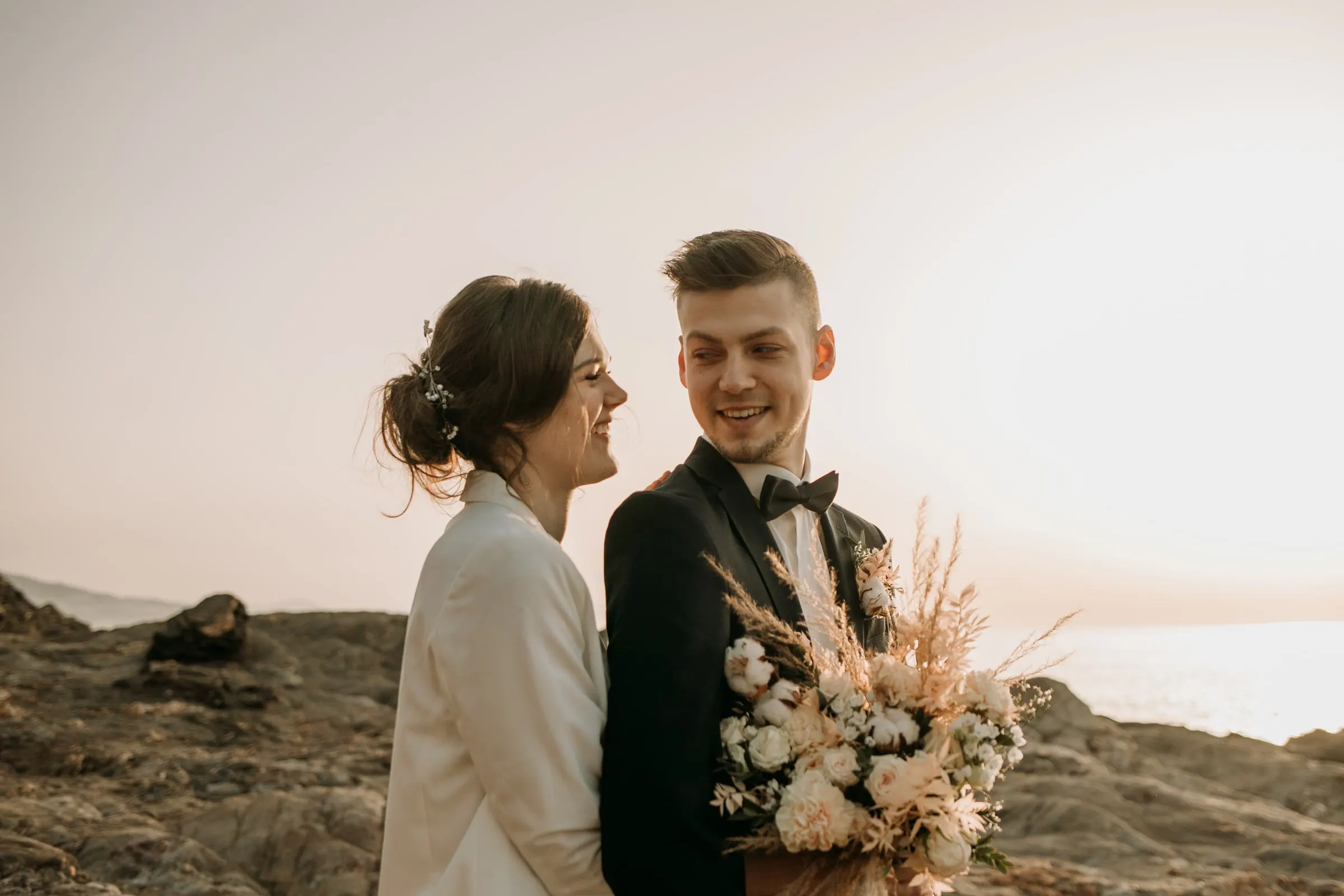 Los novios ríen juntos en la costa rocosa con la luz de la tarde