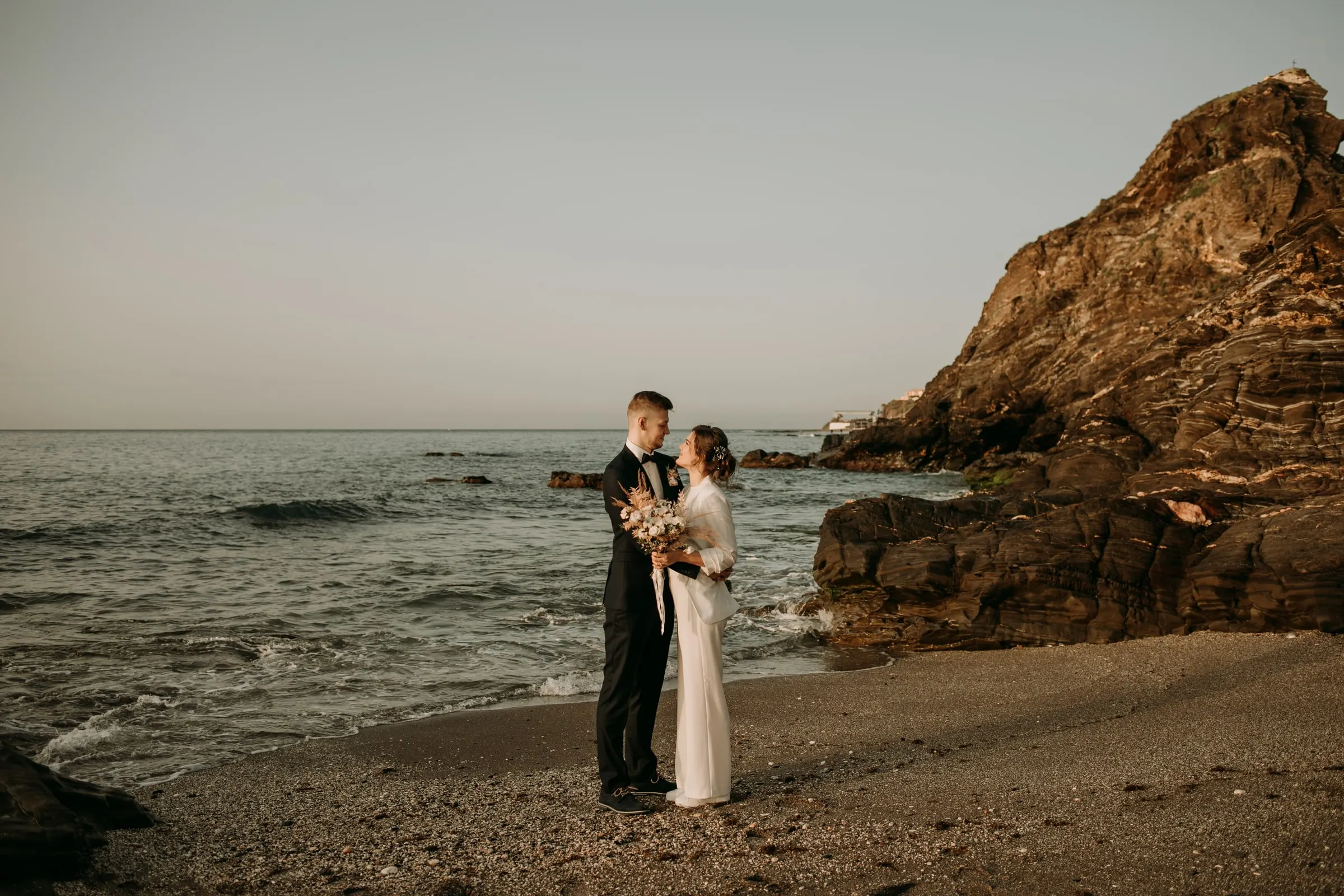Los novios en una playa de grava junto a un promontorio rocoso, postboda en la Costa del Sol
