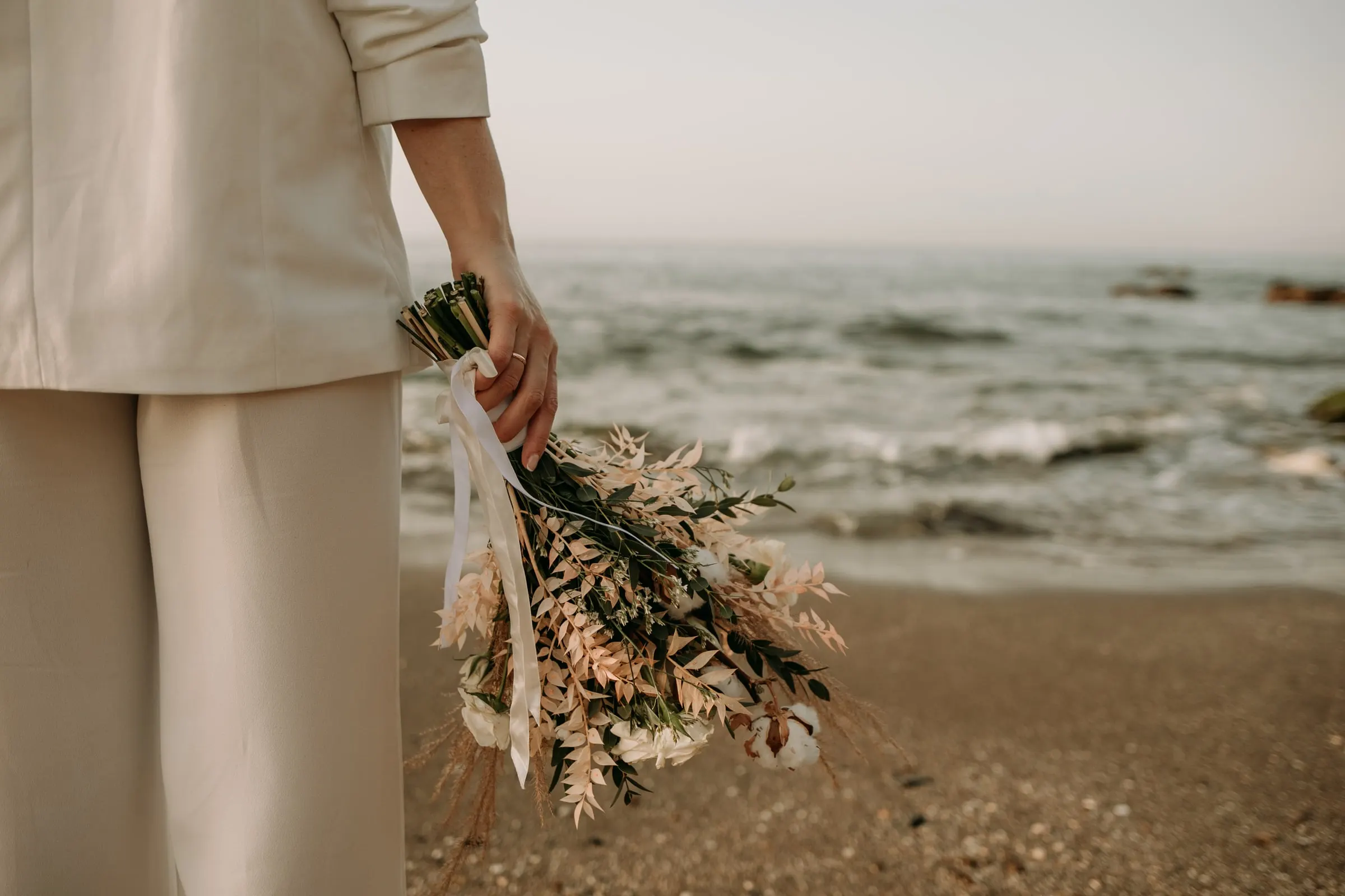 Ramo de hierbas secas y flores claras en la mano de la novia junto al mar