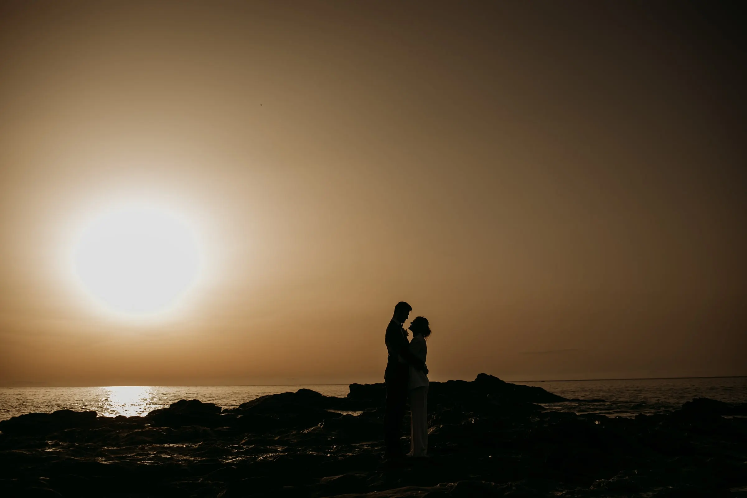 Silueta de los novios en las rocas mientras el sol se pone sobre el Mediterráneo