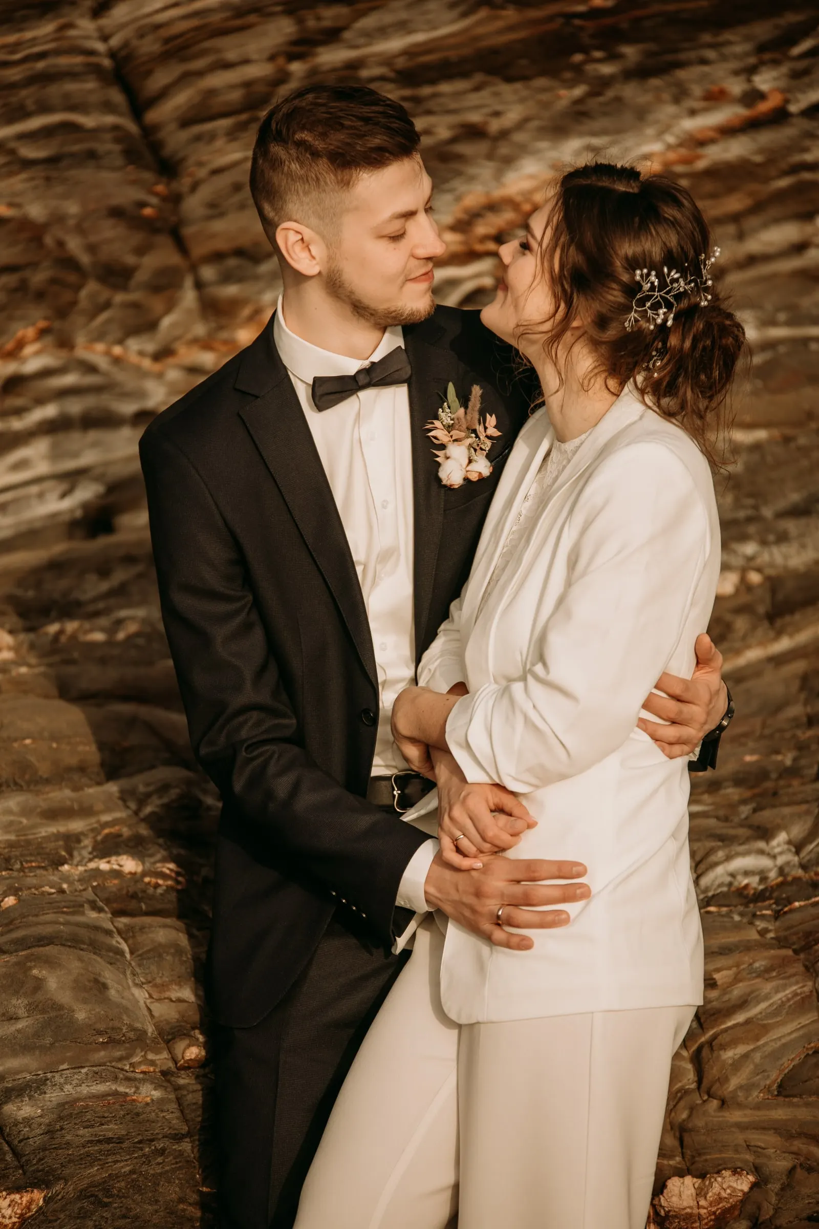 El novio besa la mejilla de la novia ante la roca veteada de la cala