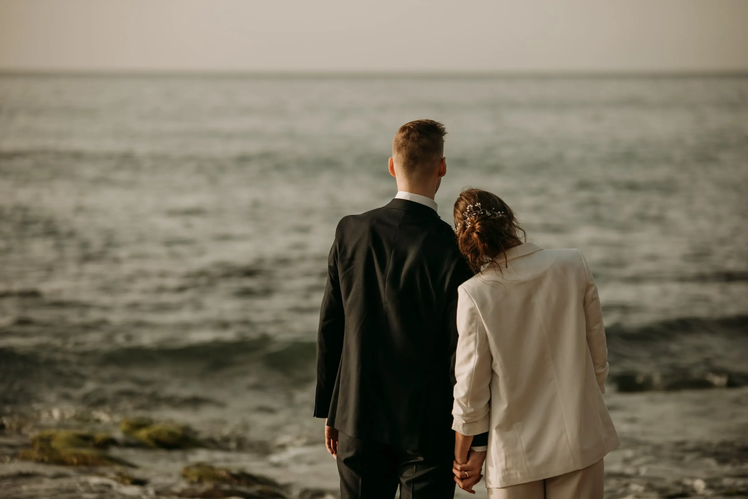Los novios de espaldas miran al mar desde la orilla