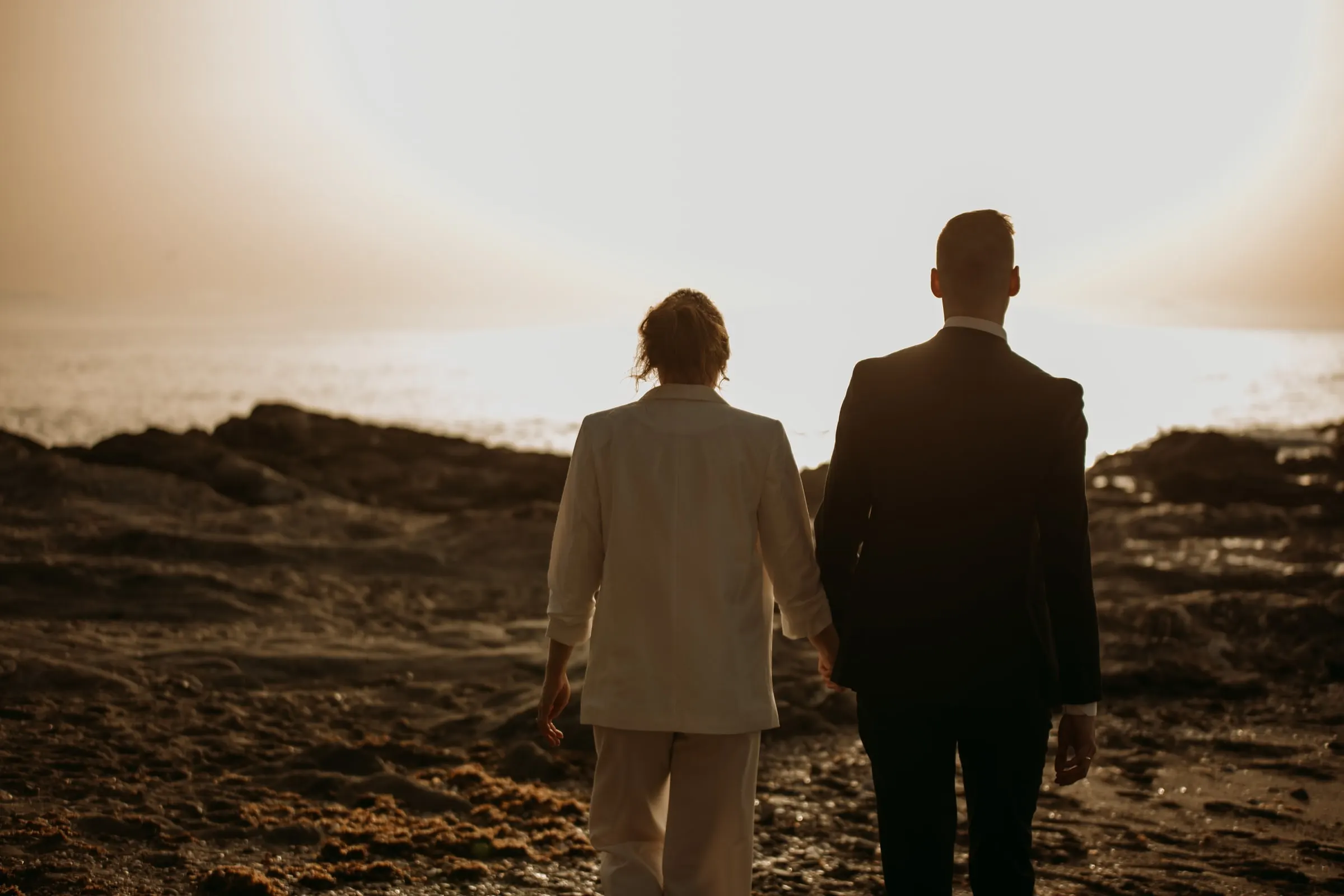 Los novios se alejan de la mano hacia el atardecer sobre las rocas