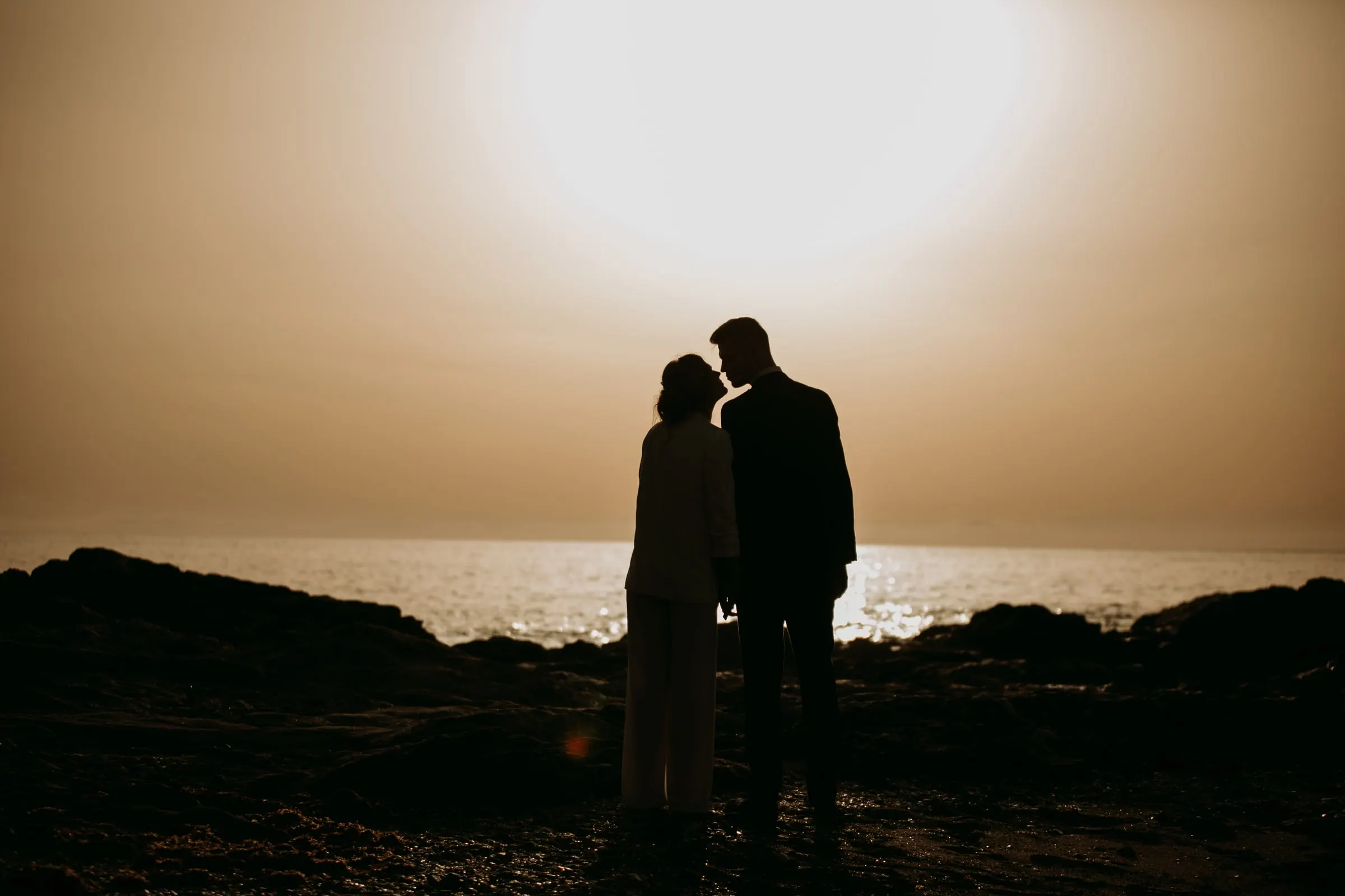 Silueta del beso de los novios en la orilla bajo un cielo encendido