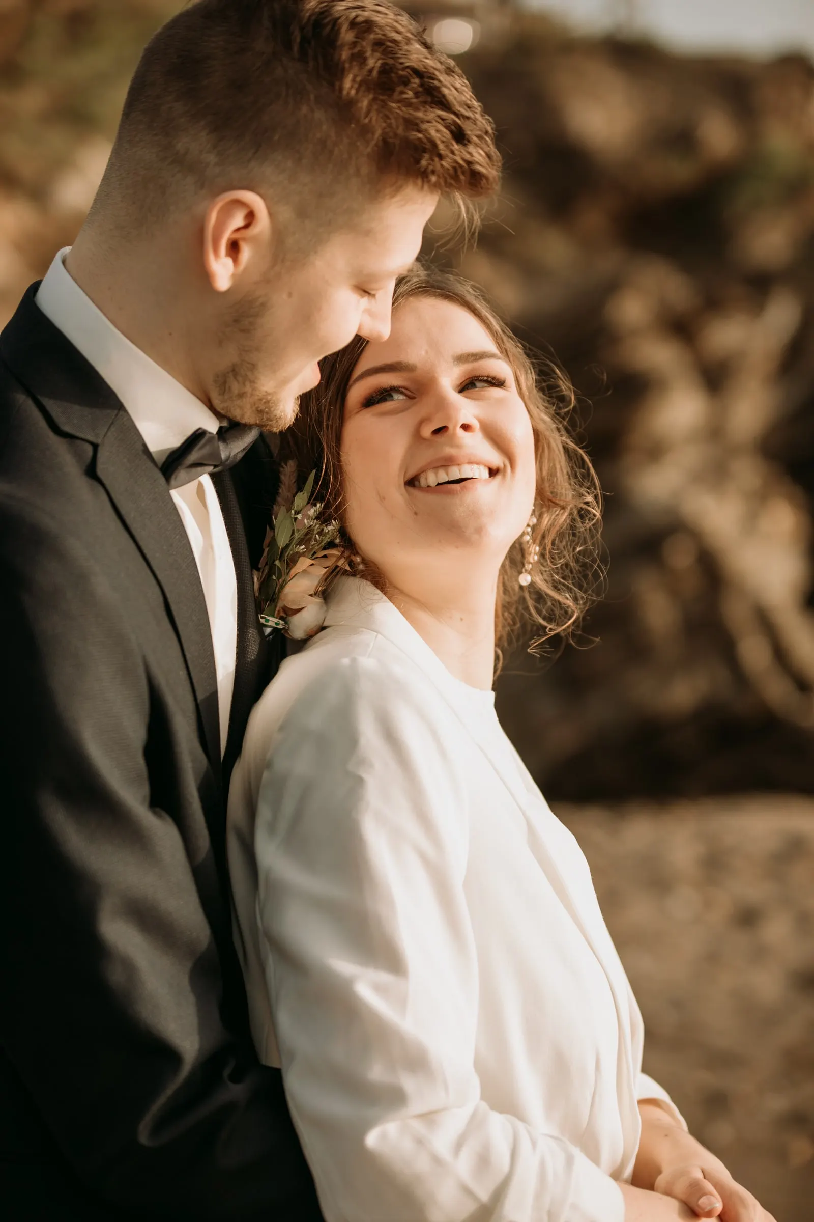 La novia ríe en brazos del novio con la luz dorada de la cala
