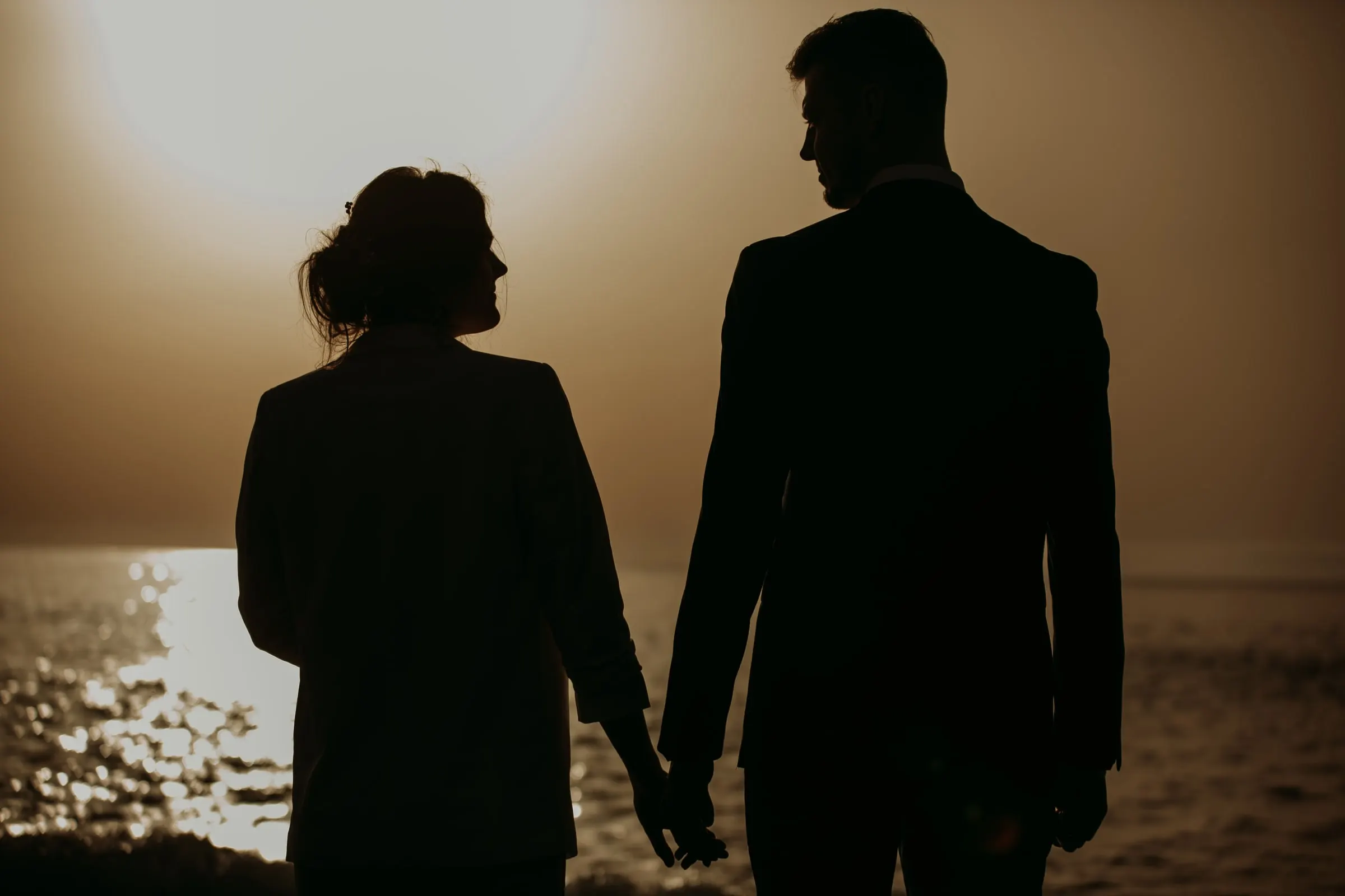 Los novios a contraluz de la mano, con el sol poniente reflejado en el mar