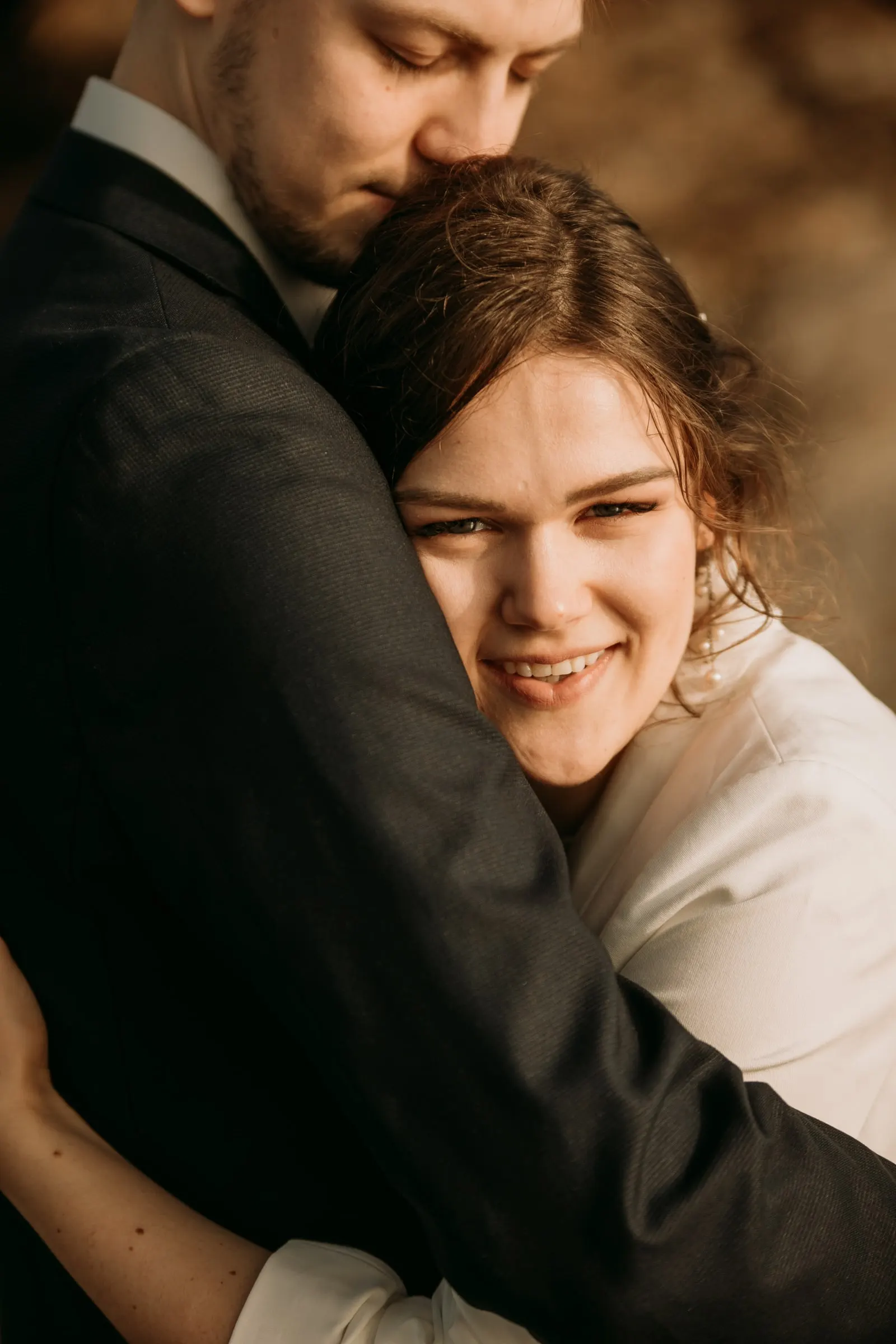 El novio abraza fuerte a la novia mientras ella sonríe a cámara
