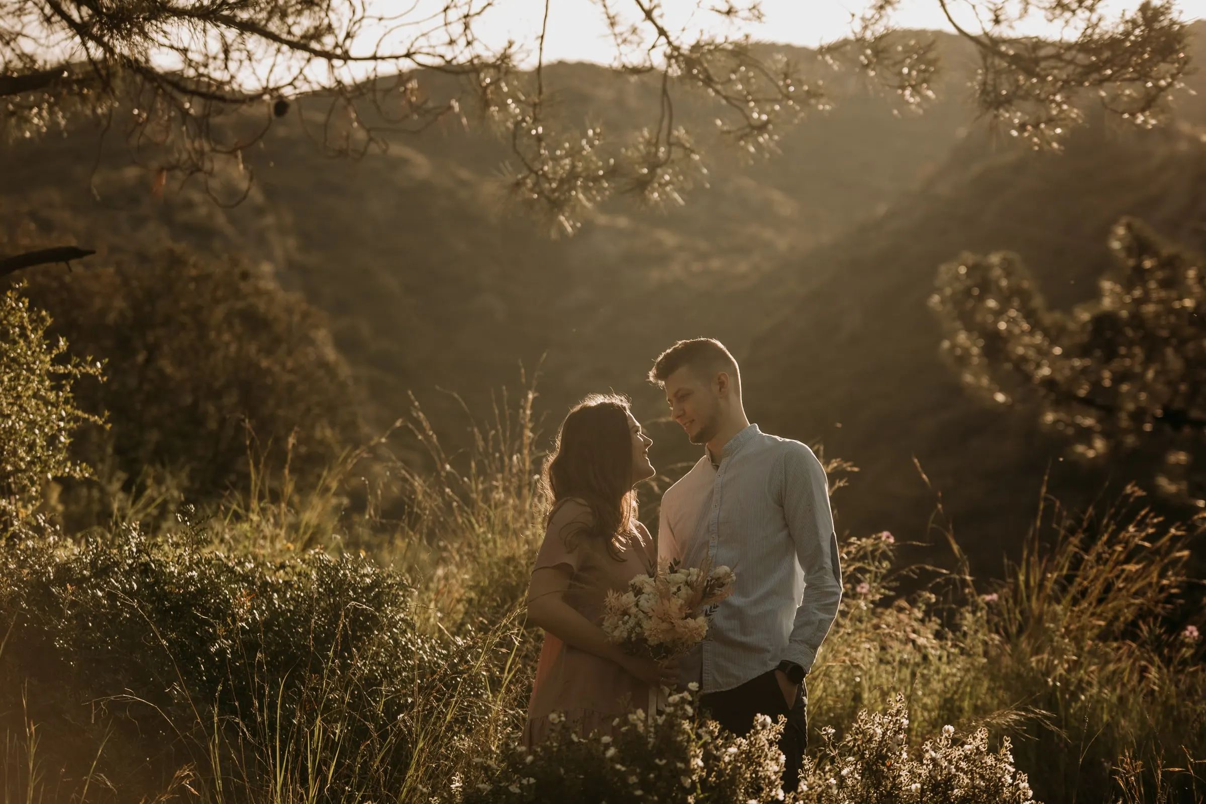 Couple standing in the tall grass of a hillside with the mountains behind, pre-wedding session on the Costa del Sol