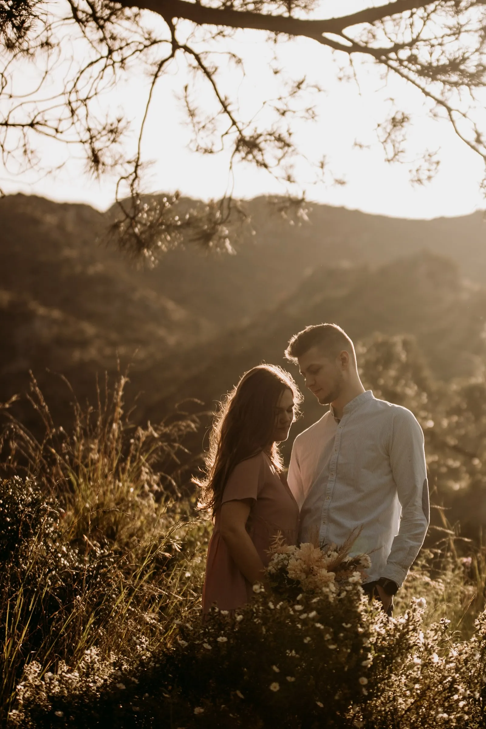 Couple face to face under a pine tree with the mountains in the distance