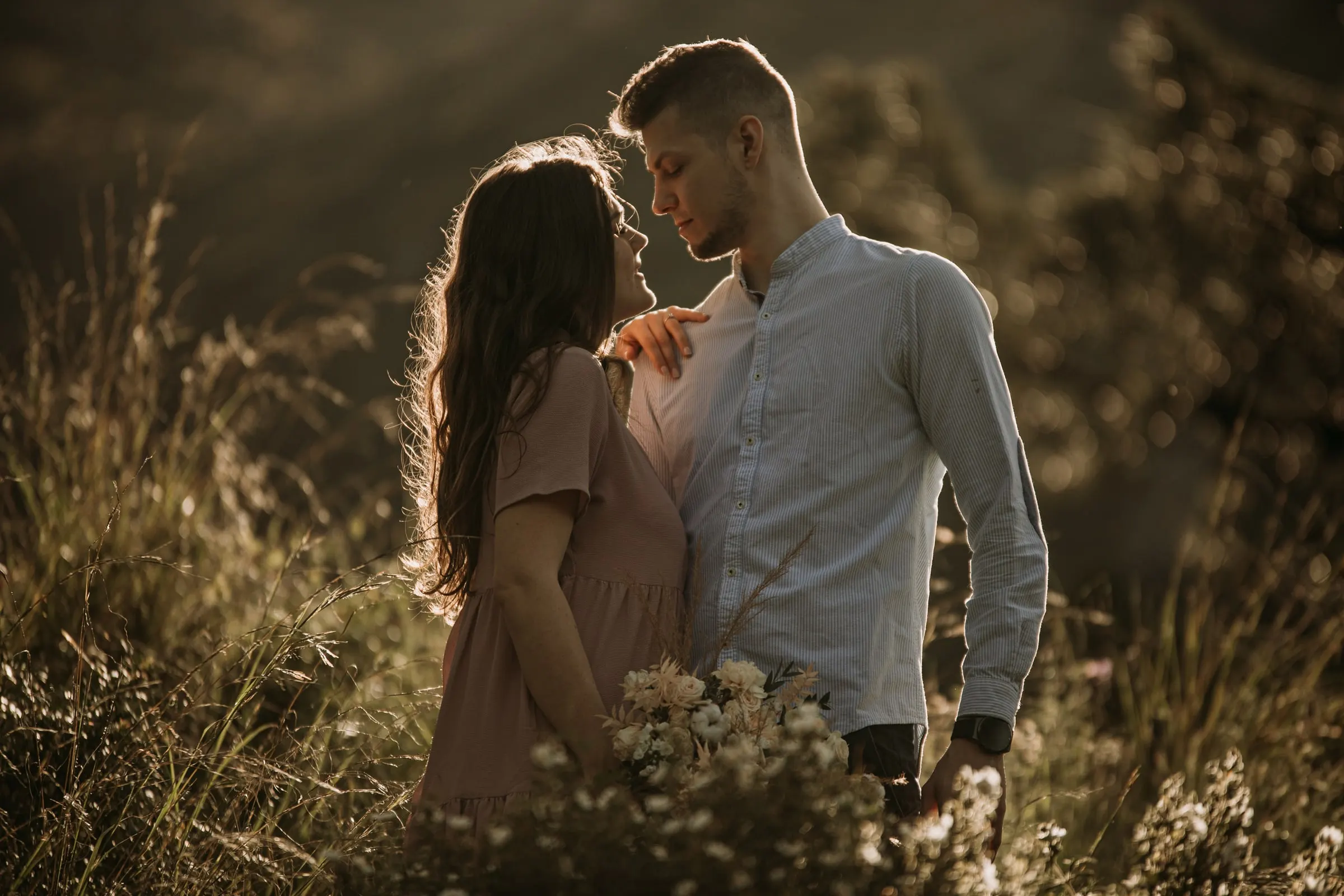 Bride-to-be looking up at her fiancé, her hand on his shoulder, in the evening light