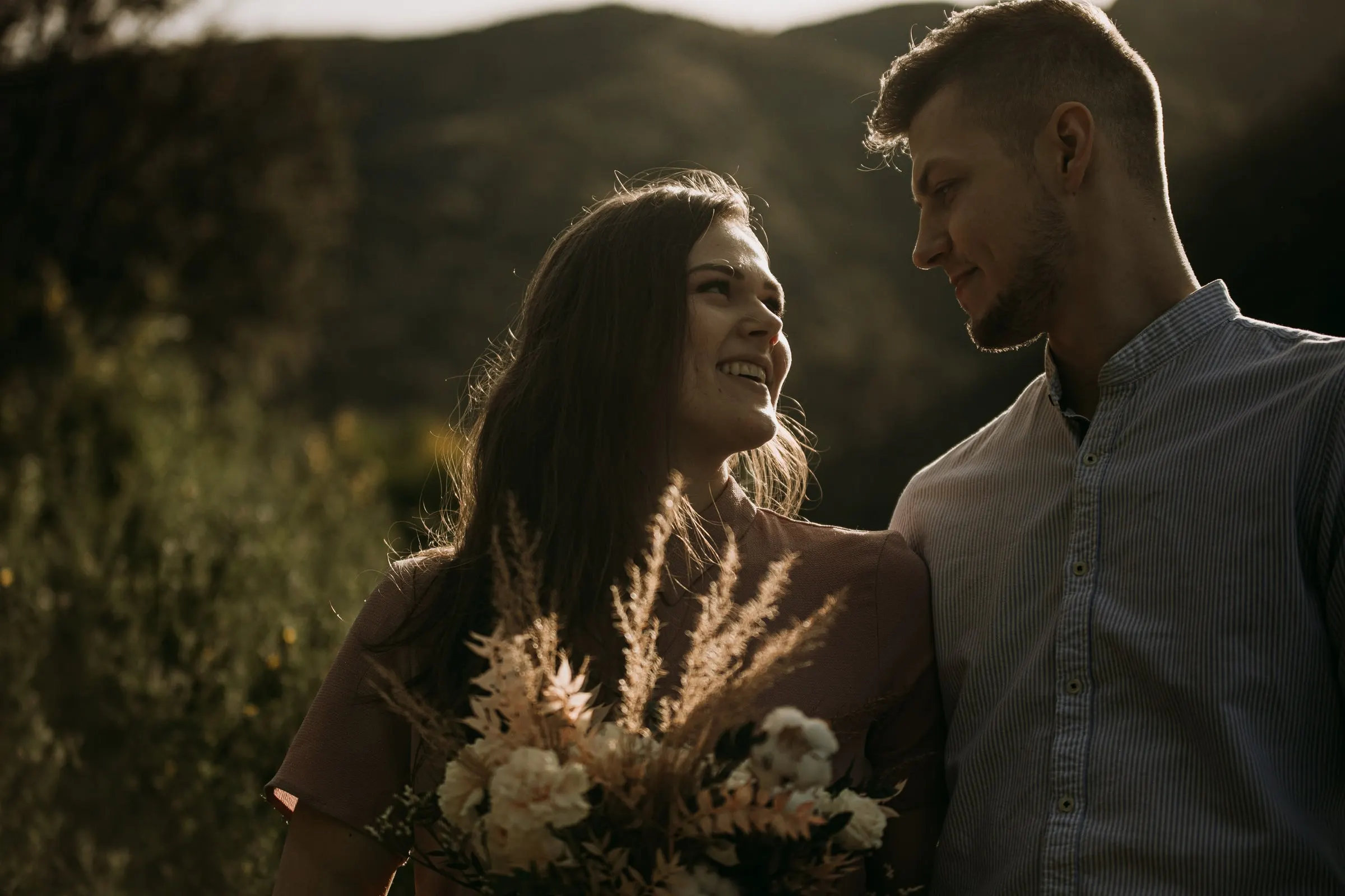 Couple laughing together with a bouquet of dried grasses, the mountains behind