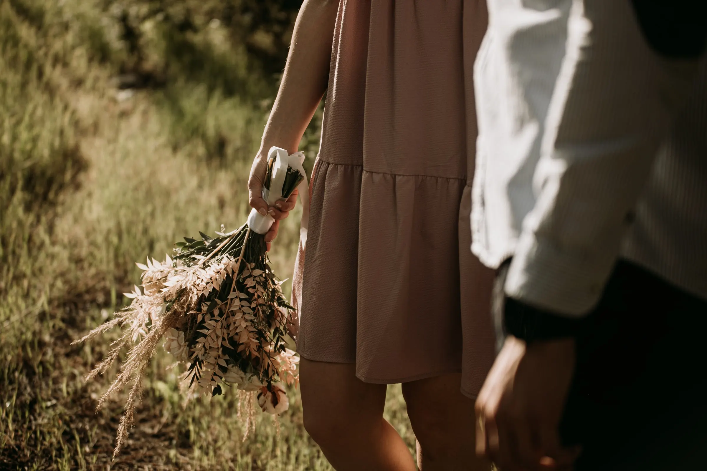 Detail of the couple walking hand in hand through the grass, the bouquet swinging