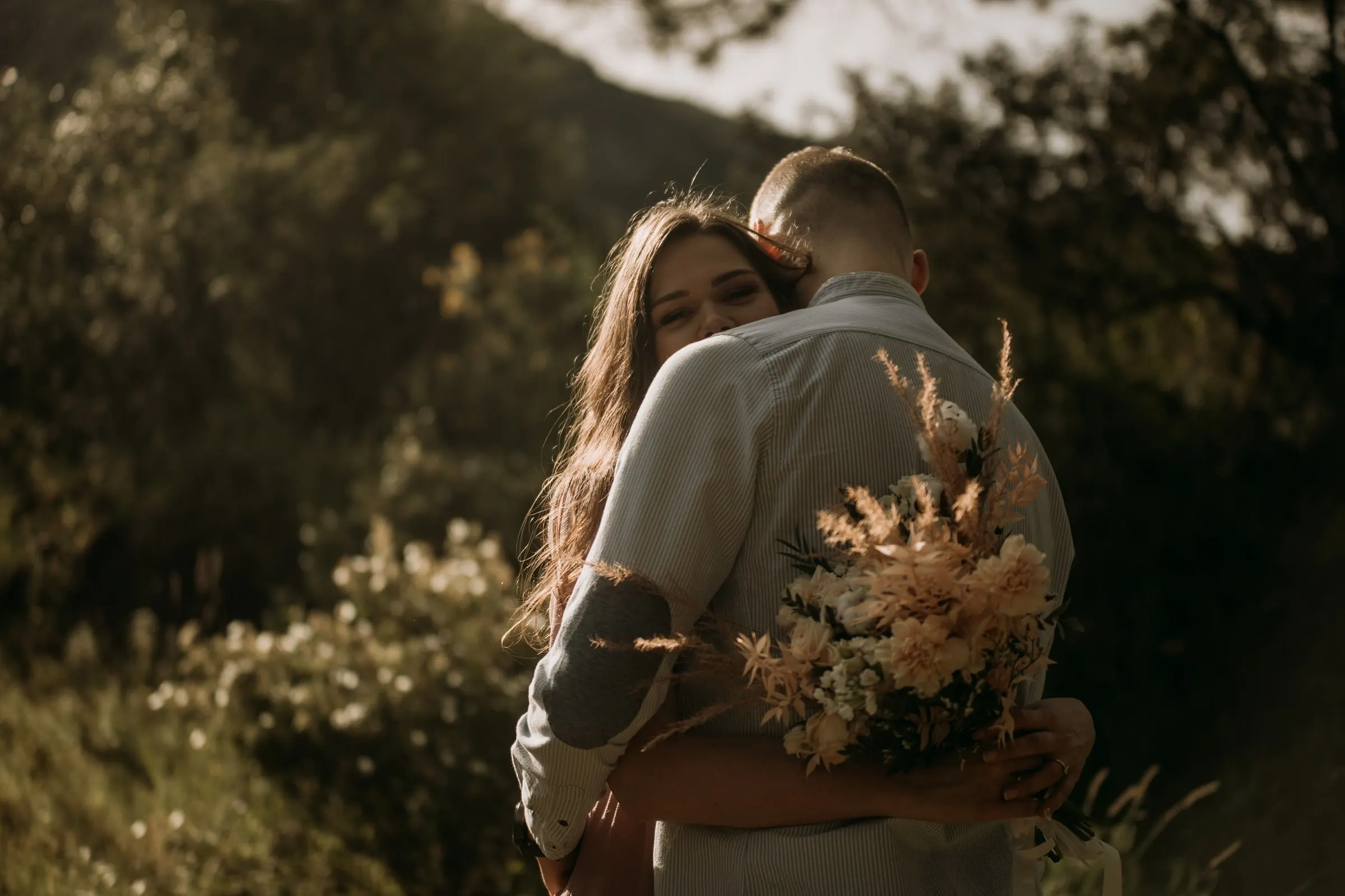 Couple embracing among green shrubs, a bouquet of pampas grass in her hand