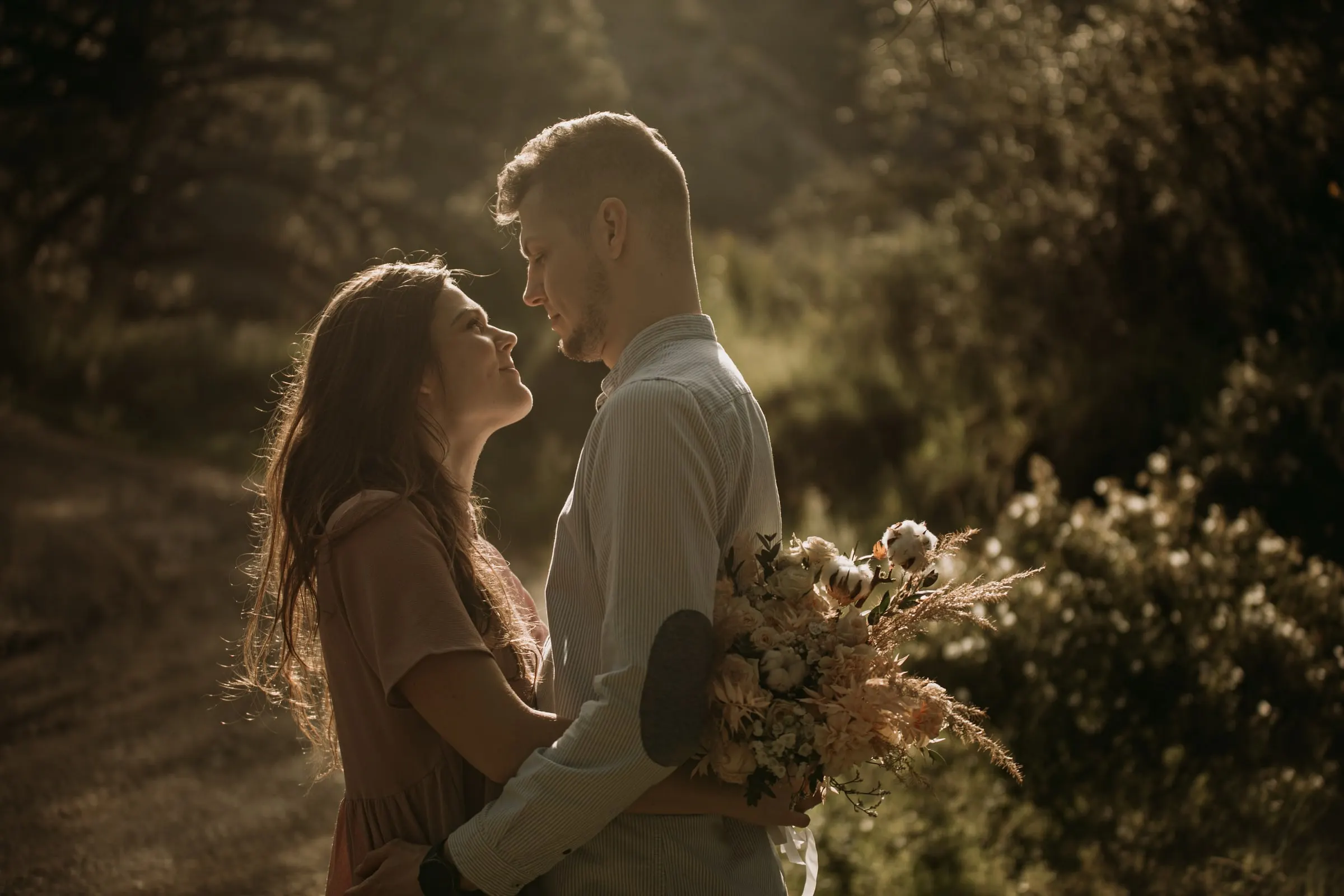 Couple face to face in a clearing among the bushes, golden backlight