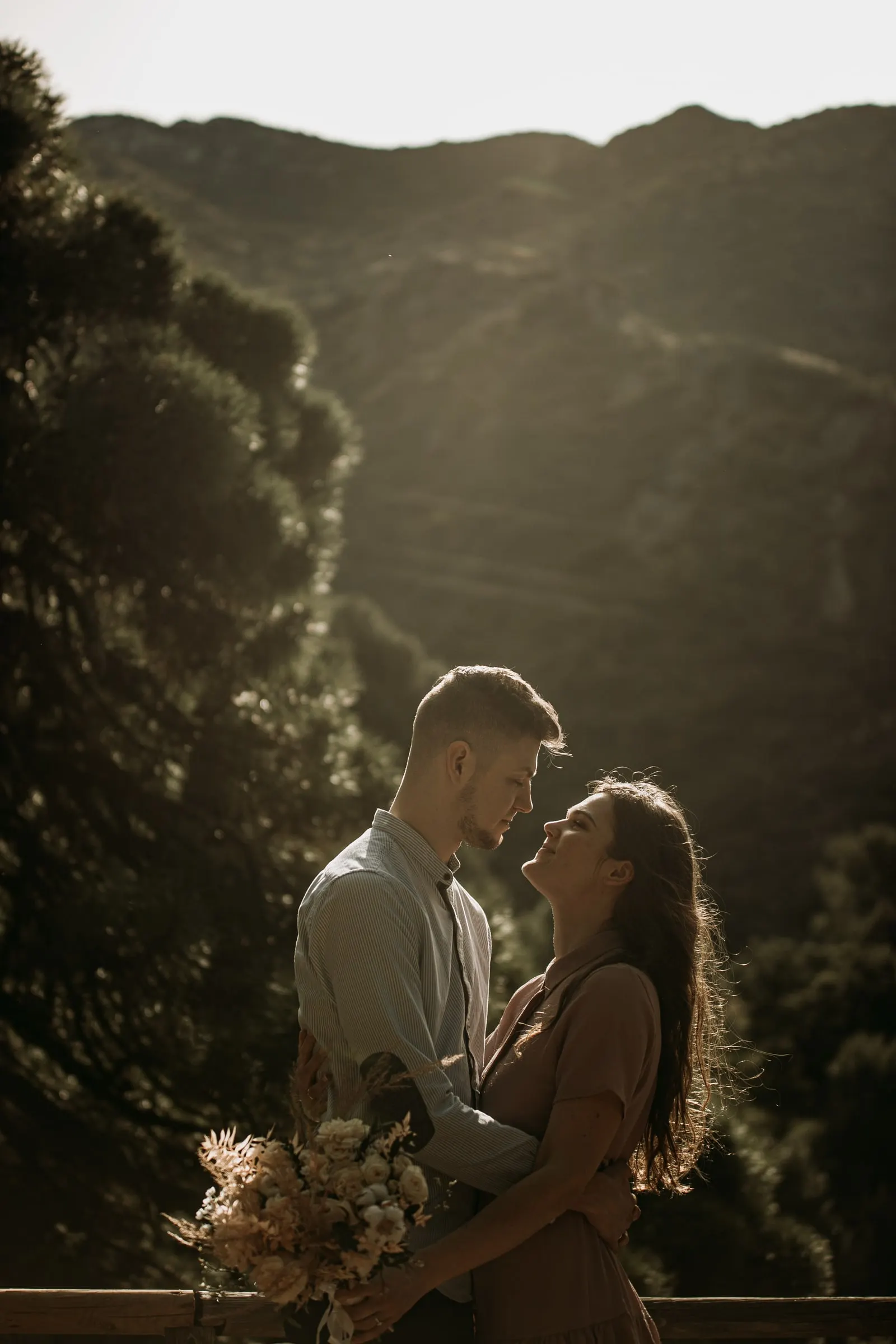 Couple face to face holding their bouquet, the mountainside behind