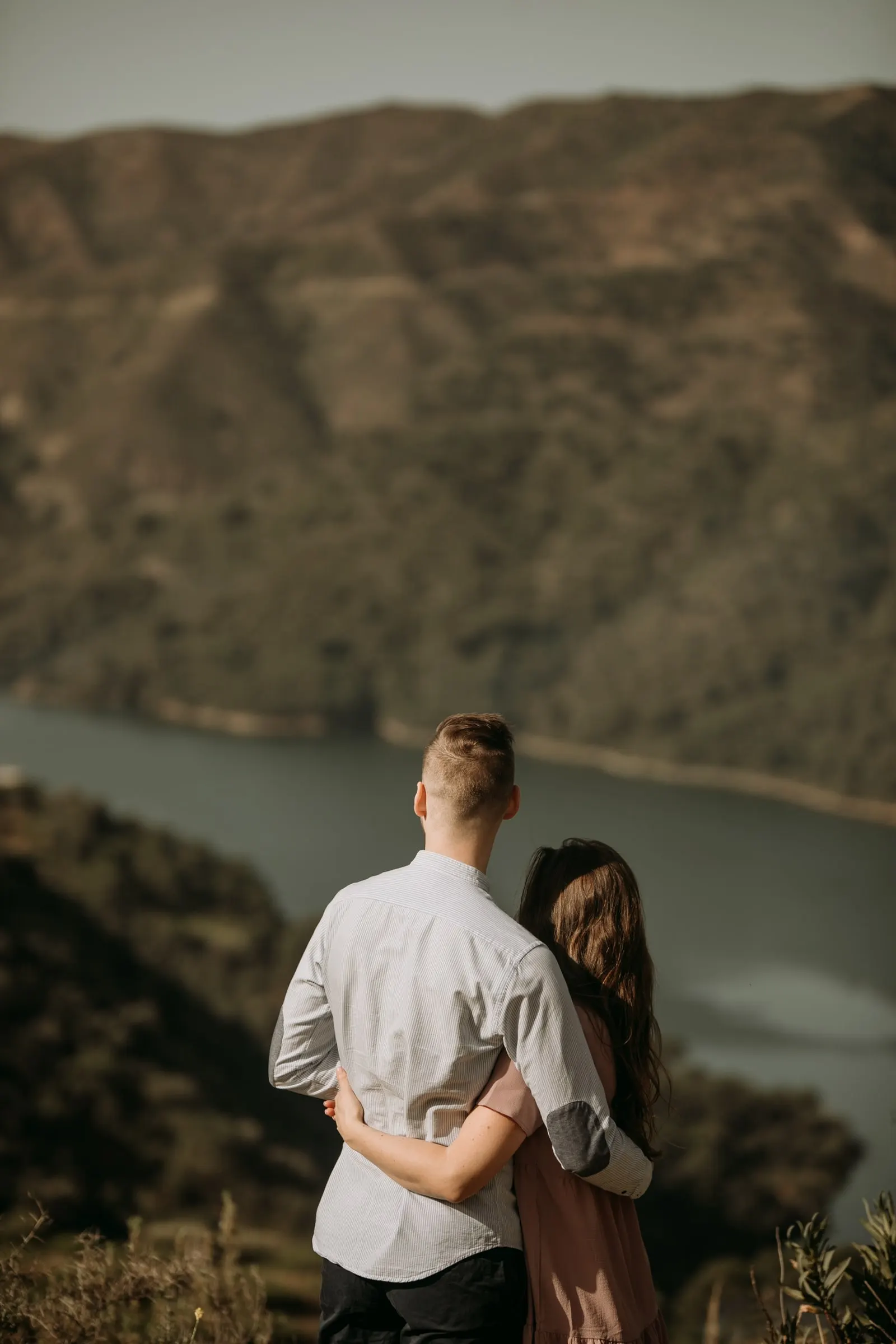 Couple from behind, embracing above the reservoir valley