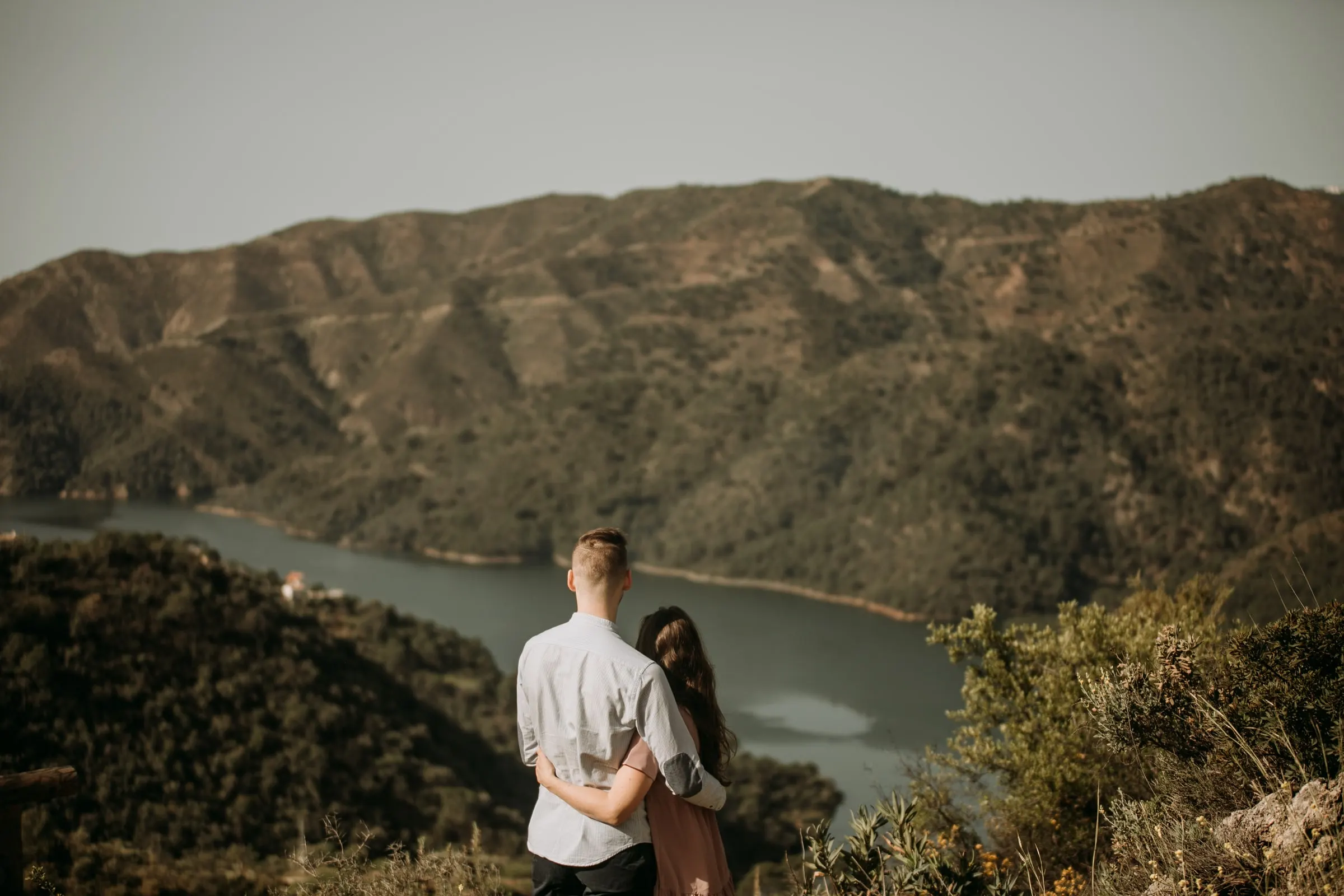 La pareja de espaldas contempla un embalse que serpentea entre montes arbolados