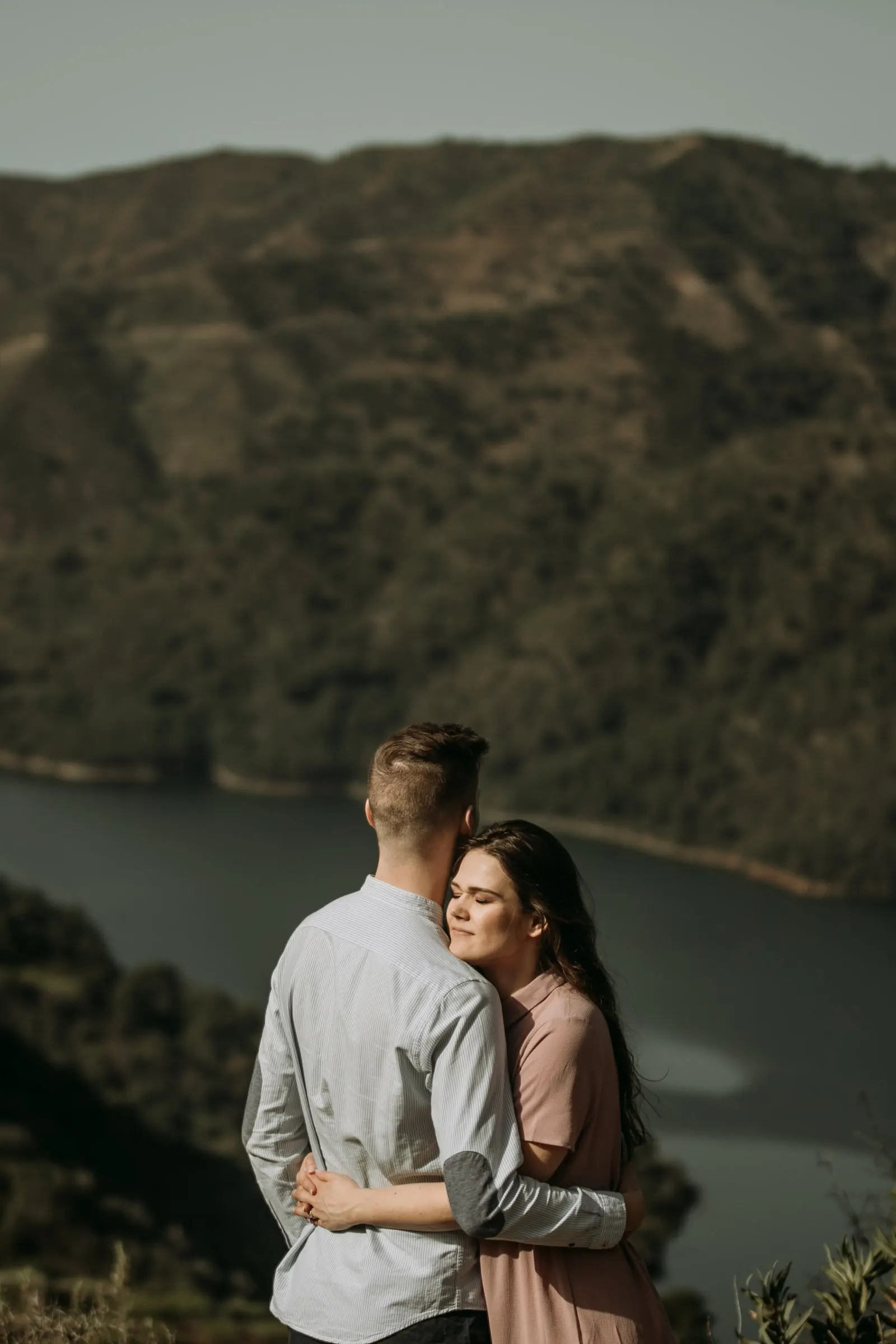 Couple embracing at a viewpoint above the water, her head resting on him