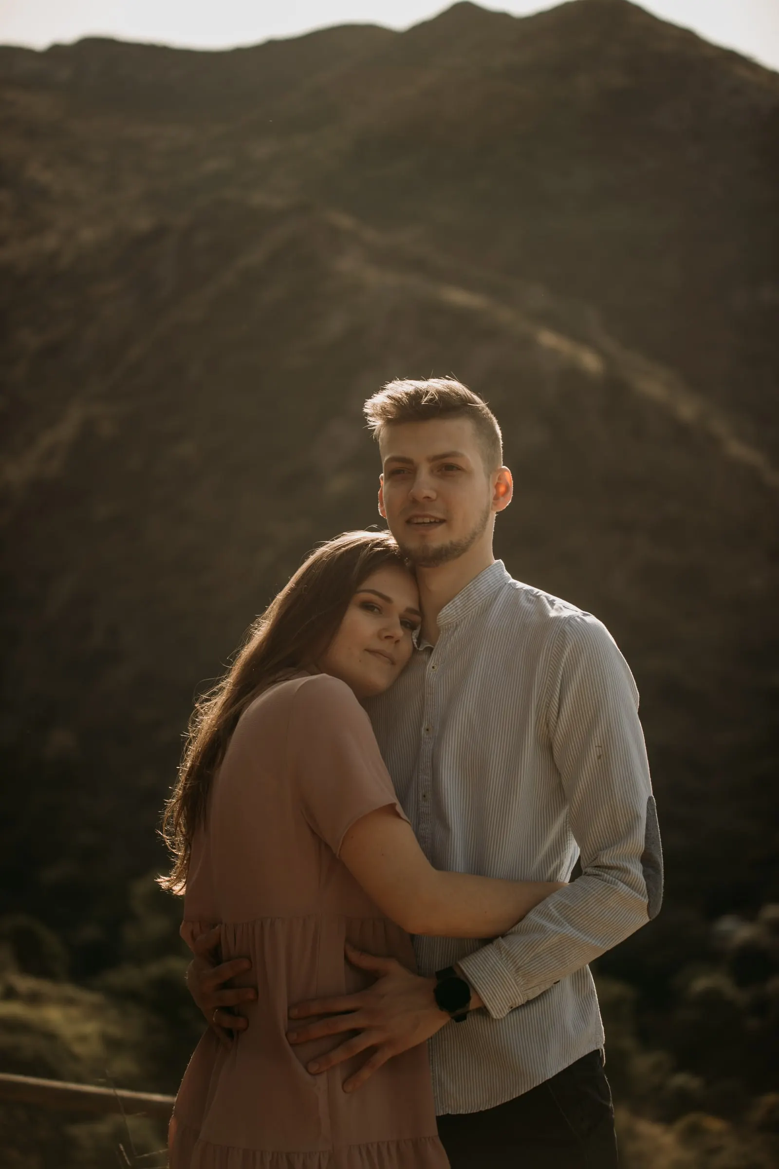 Couple embracing and smiling at the camera with a mountain behind
