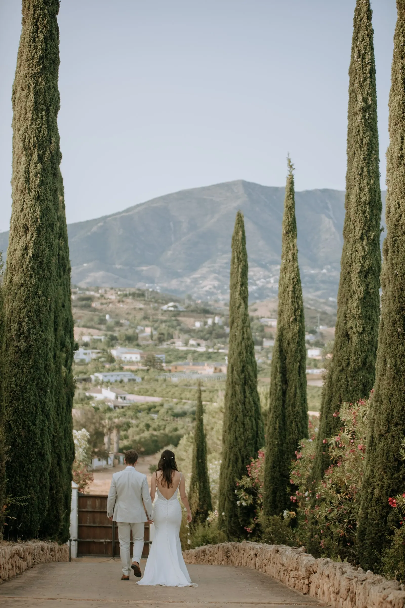 Novios caminando por un camino de cipreses con la sierra al fondo, boda en Málaga