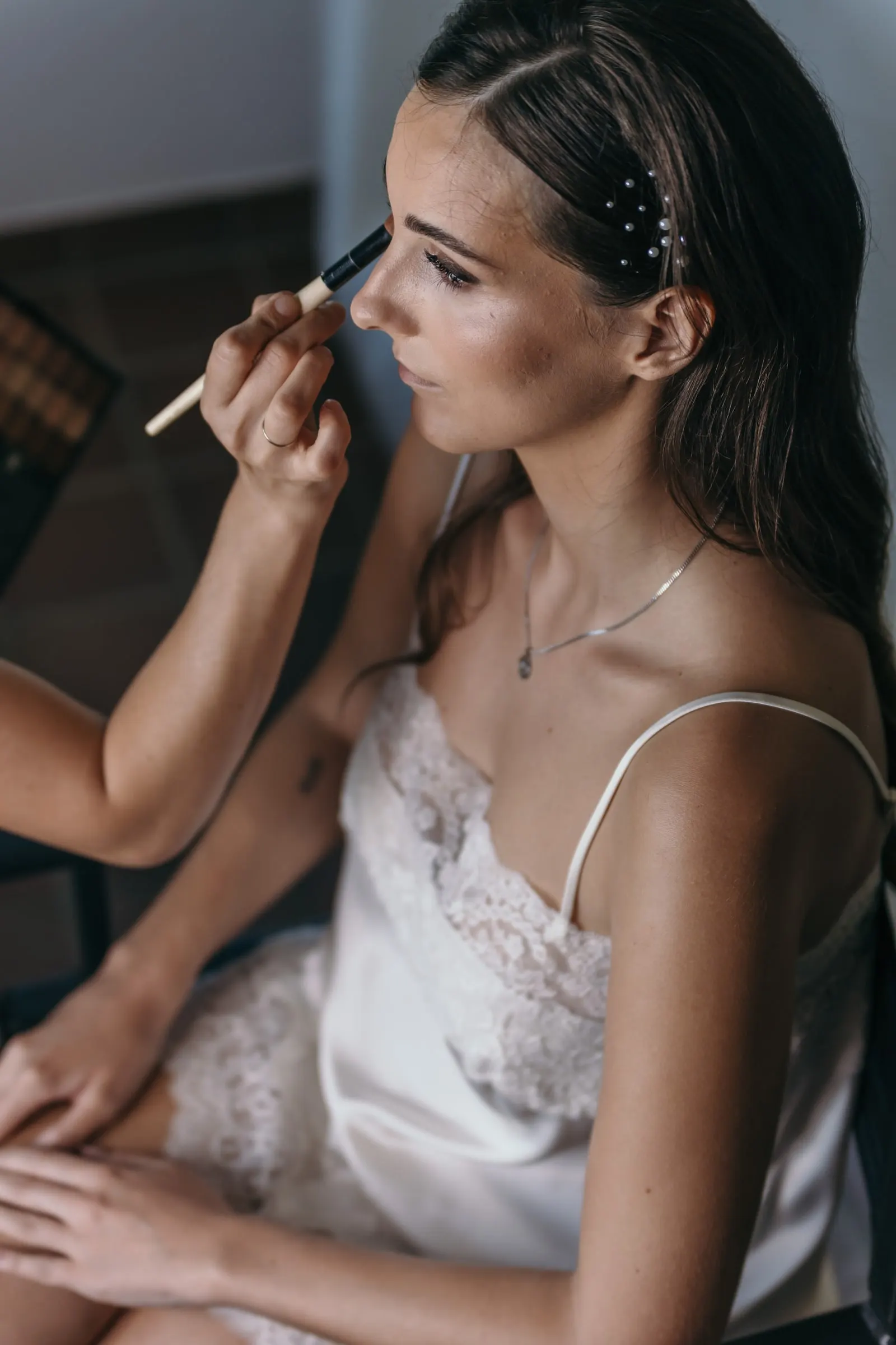 Make-up artist brushing the bride's eyelid, pearl pins in her hair