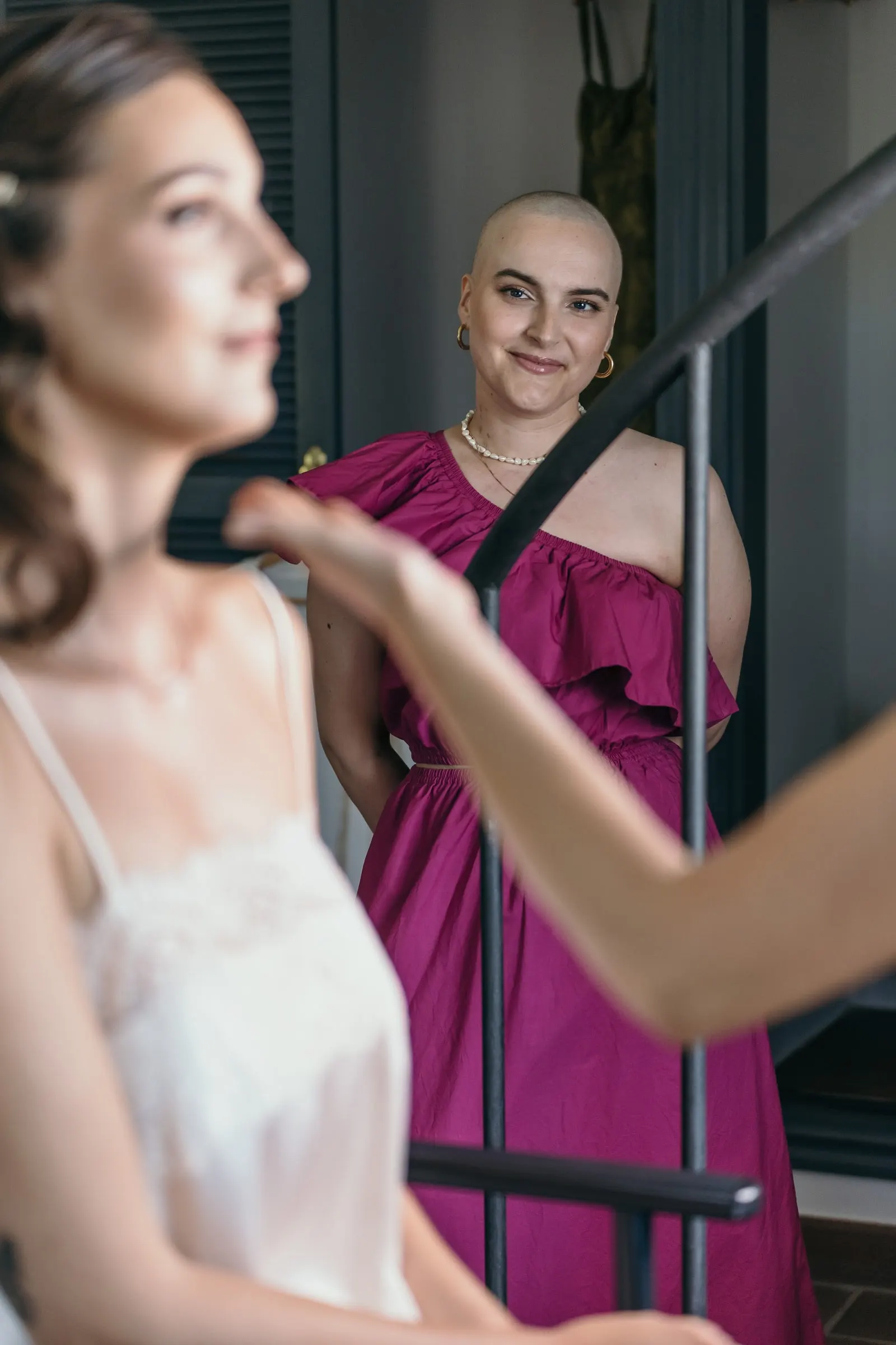 Friend in a magenta ruffled dress watching the bride get ready by the staircase