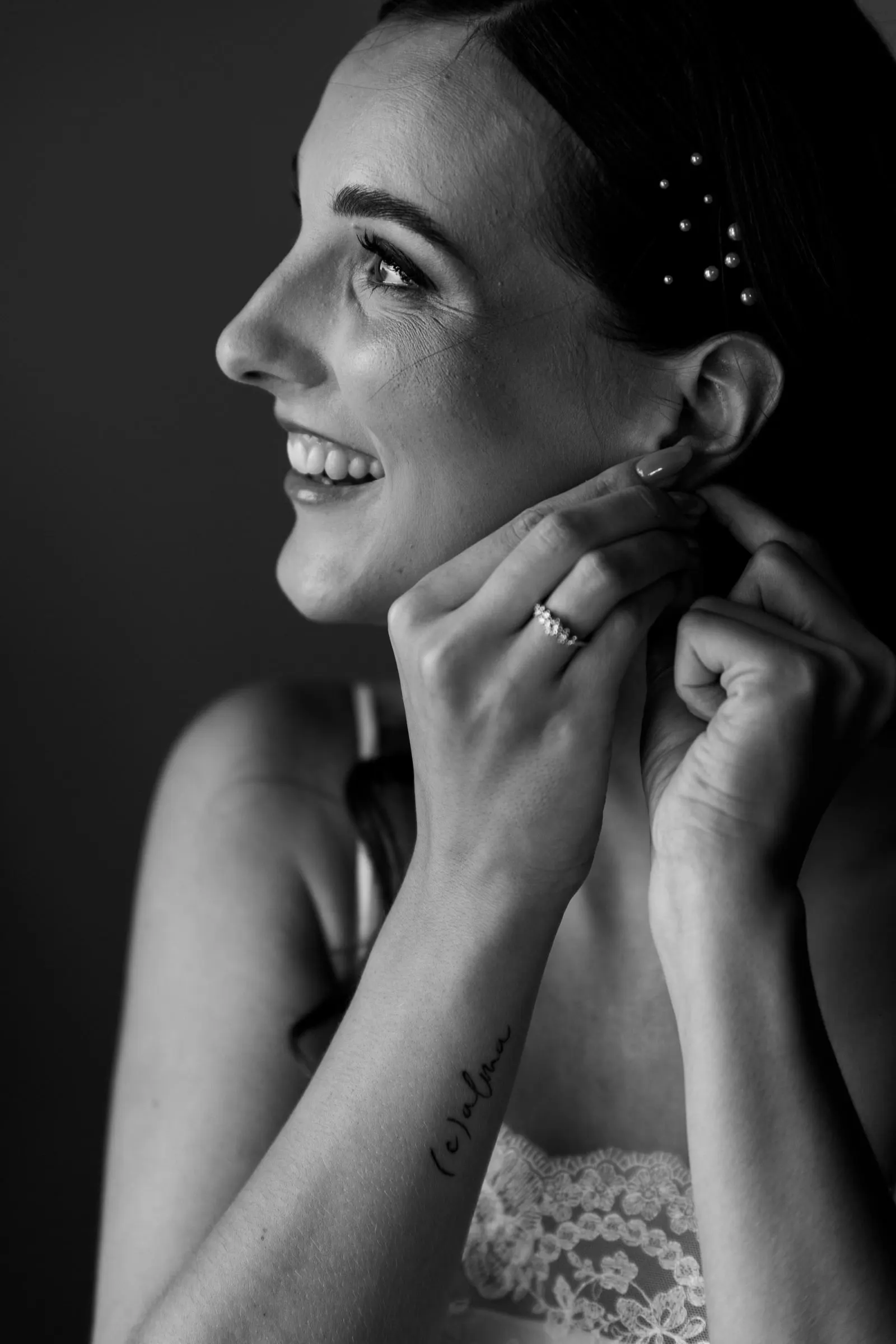 Black and white portrait of the bride putting on an earring and smiling