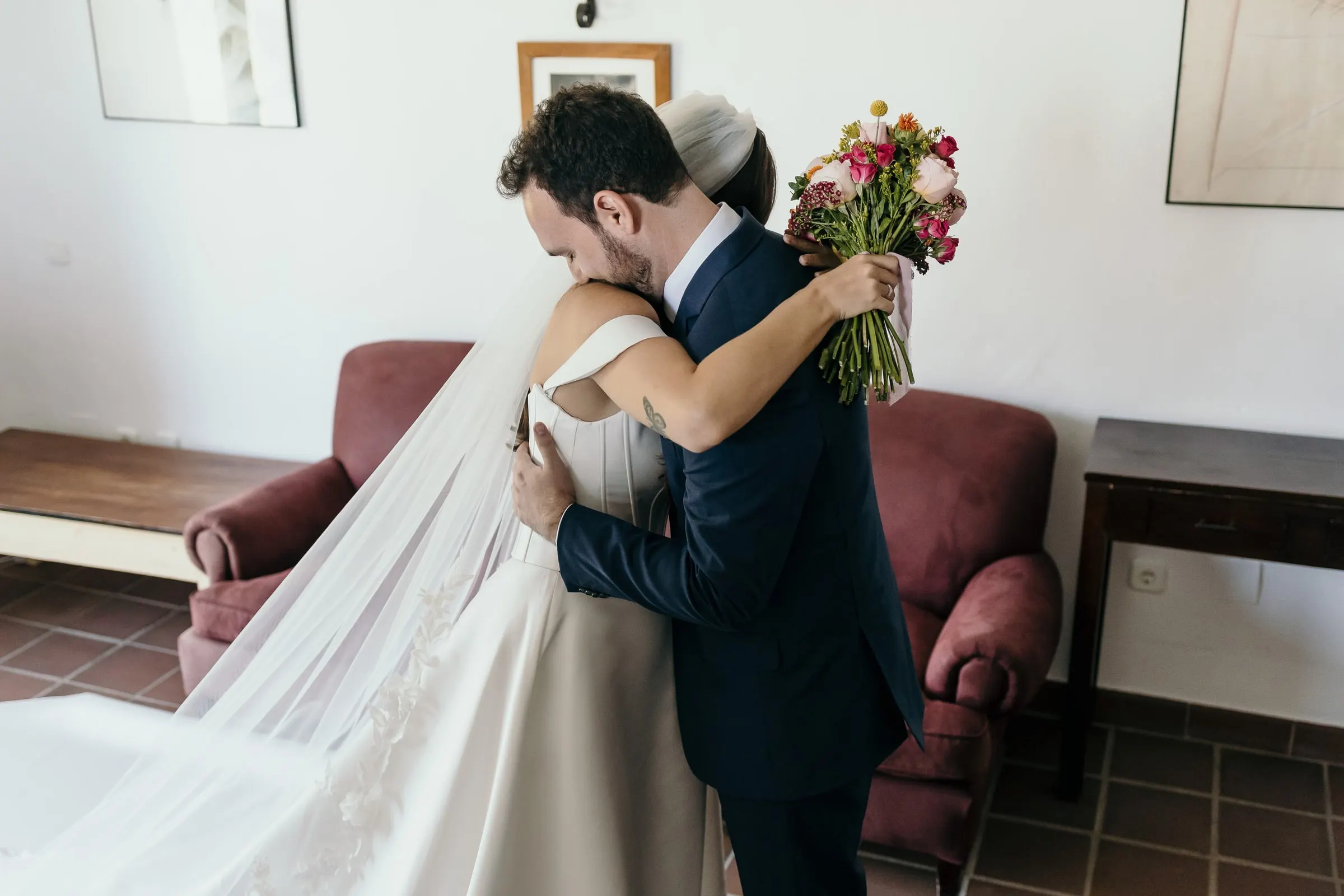 Groom hugging the bride, her bouquet of pink and orange flowers over his shoulder