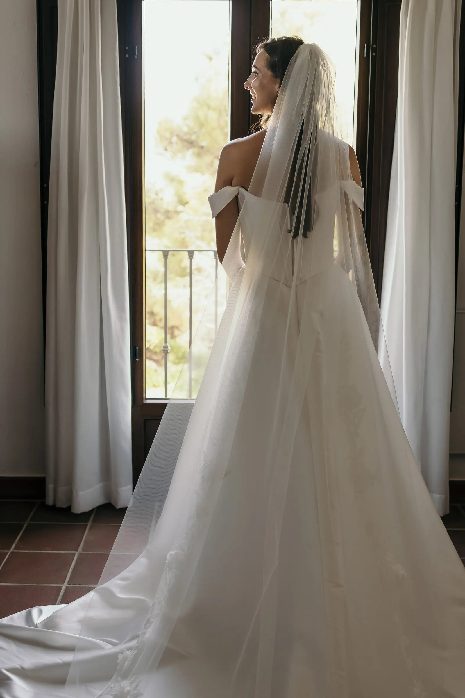 Bride with her long veil and train looking out of a tall window