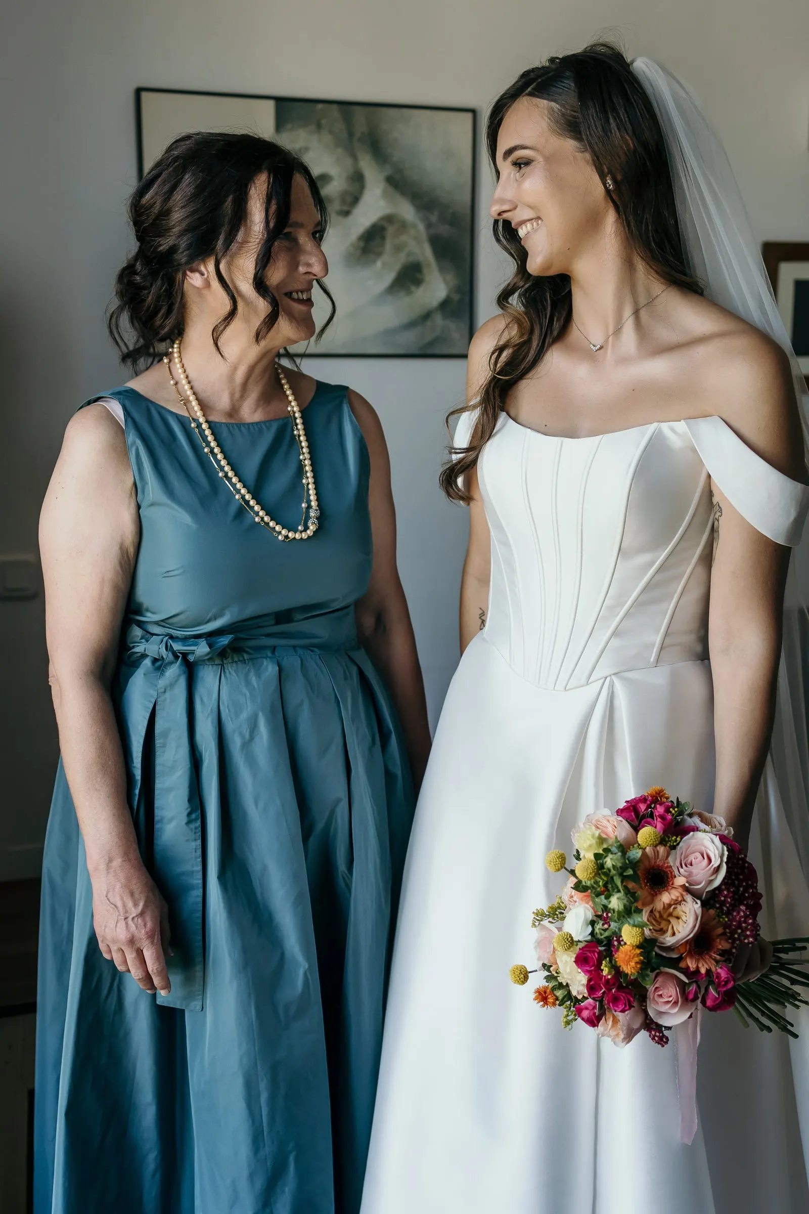 Bride with her bouquet smiling at the woman in the teal dress before the ceremony