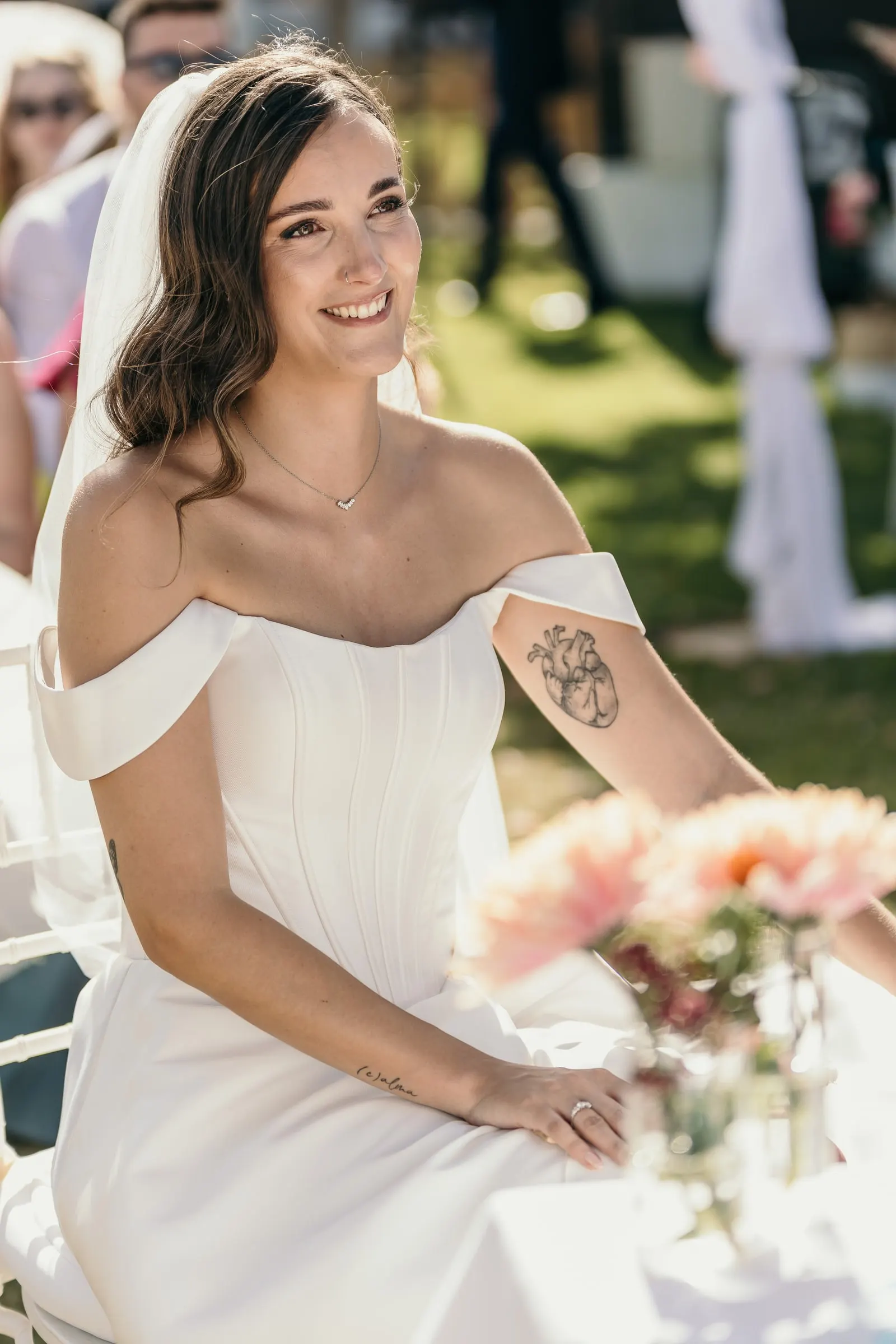 Bride smiling in her seat at the ceremony, a tattoo on her upper arm