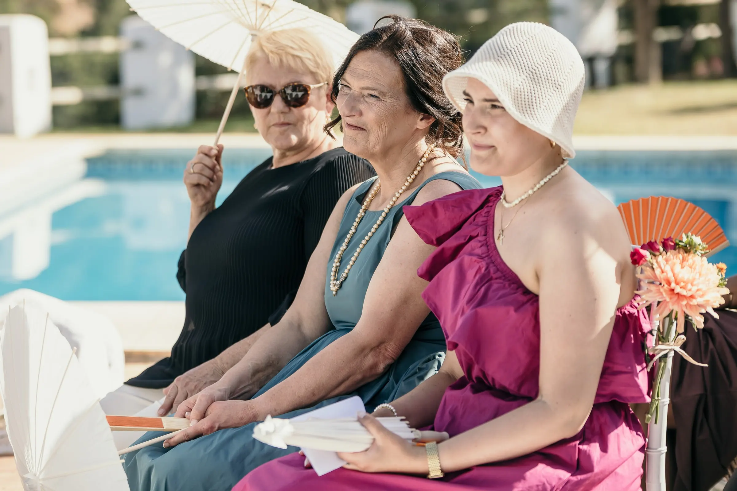 Three women watching the ceremony from the front row beside the swimming pool