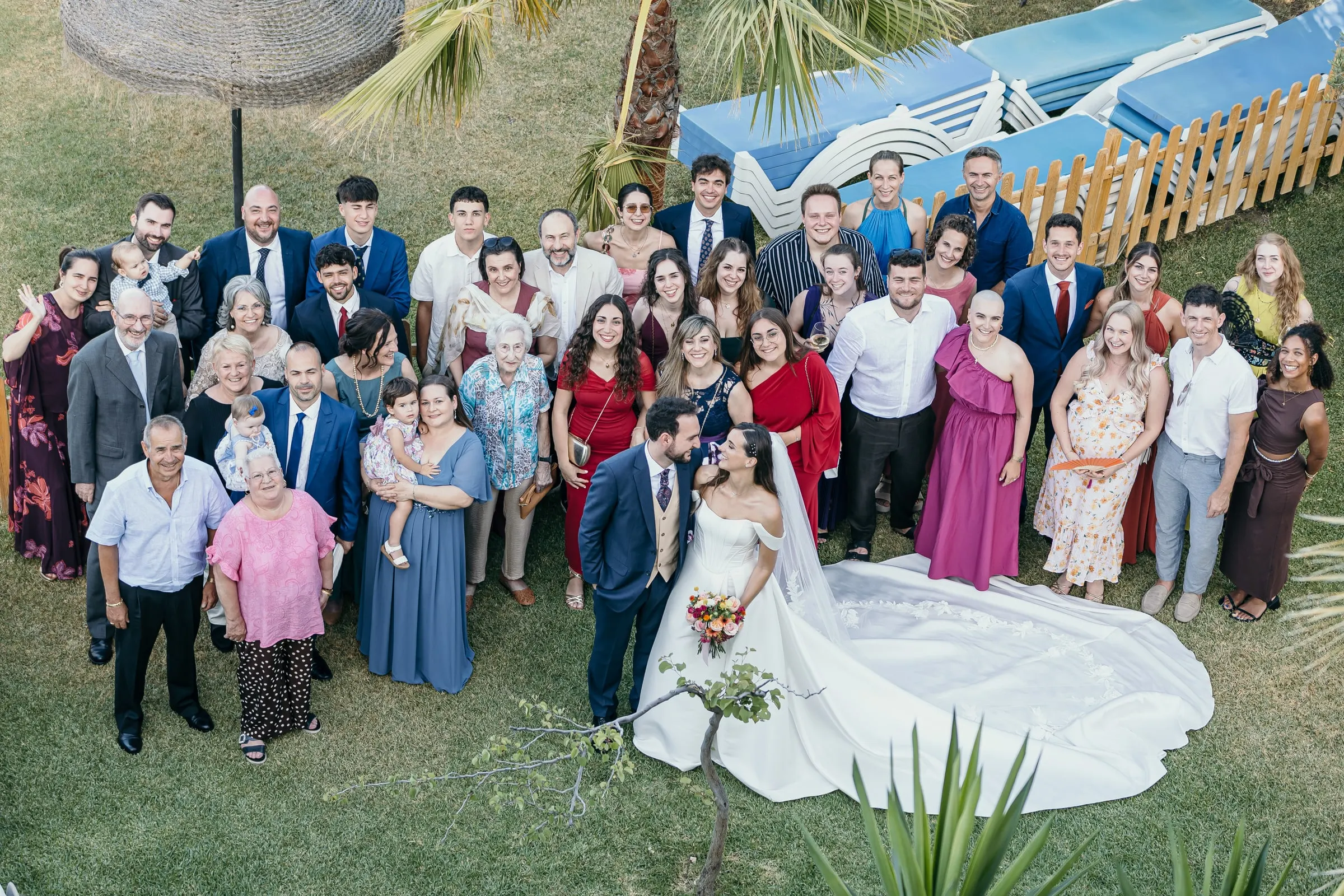 Group photo from above of the couple with all their guests on the lawn by the pool loungers