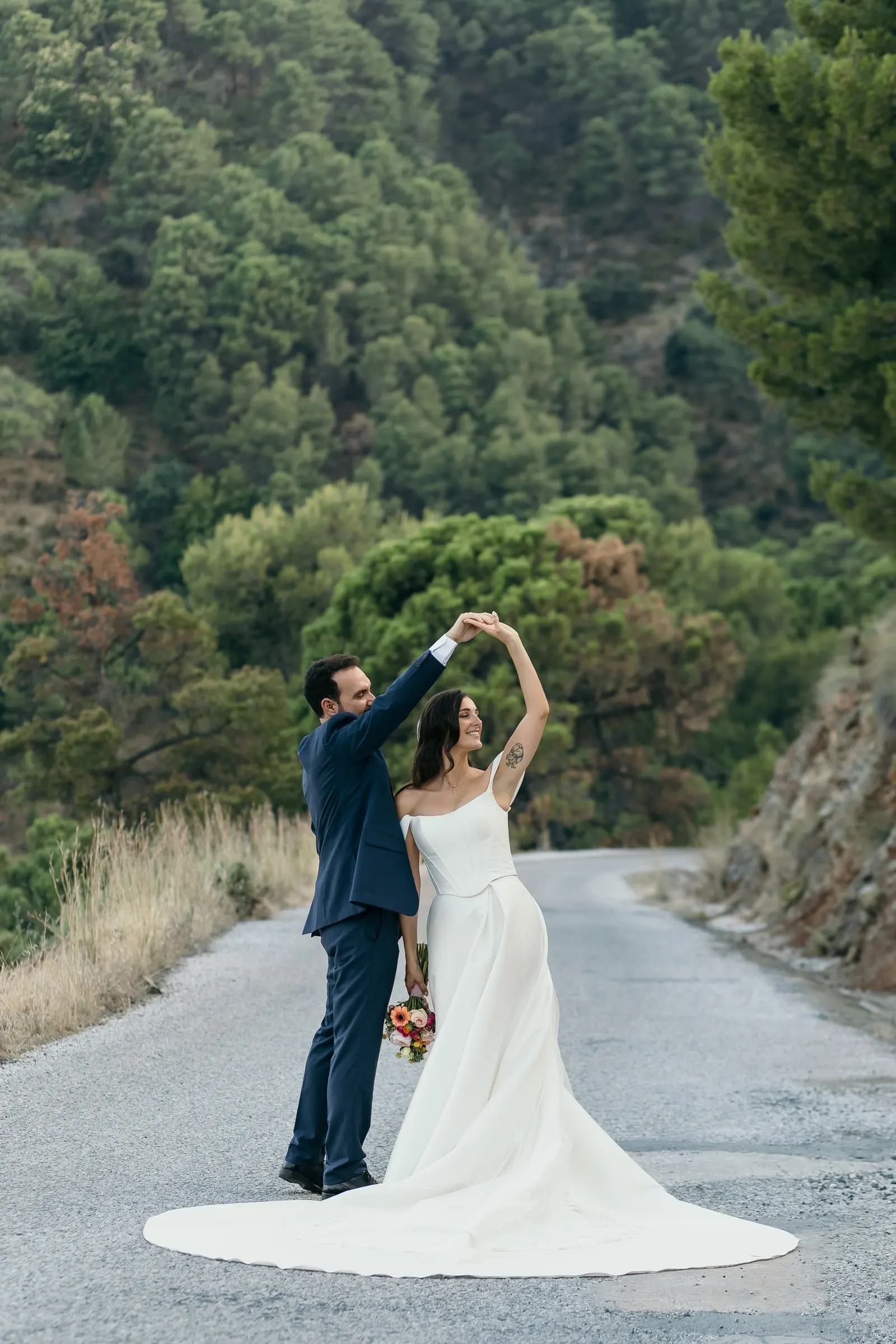 Groom twirling the bride on a quiet mountain road among the pines